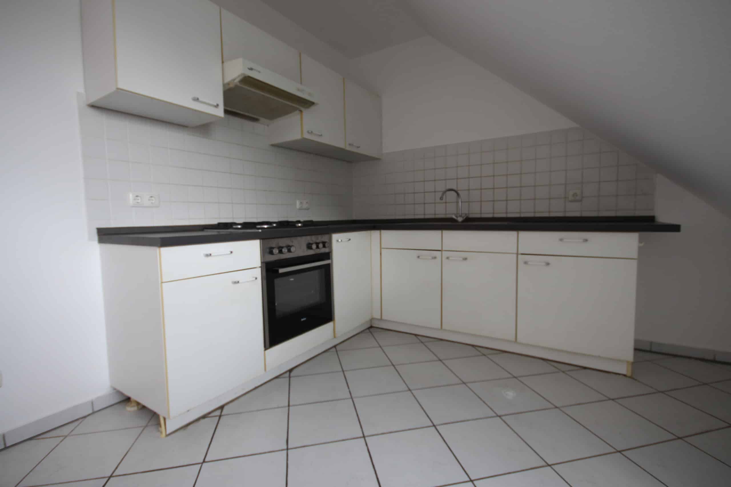 Dachgeschosswohnung Einbauküche in L-Form mit weißen Oberschränken, schwarzer Arbeitsplatte, Fliesenspiegel und Dachschräge