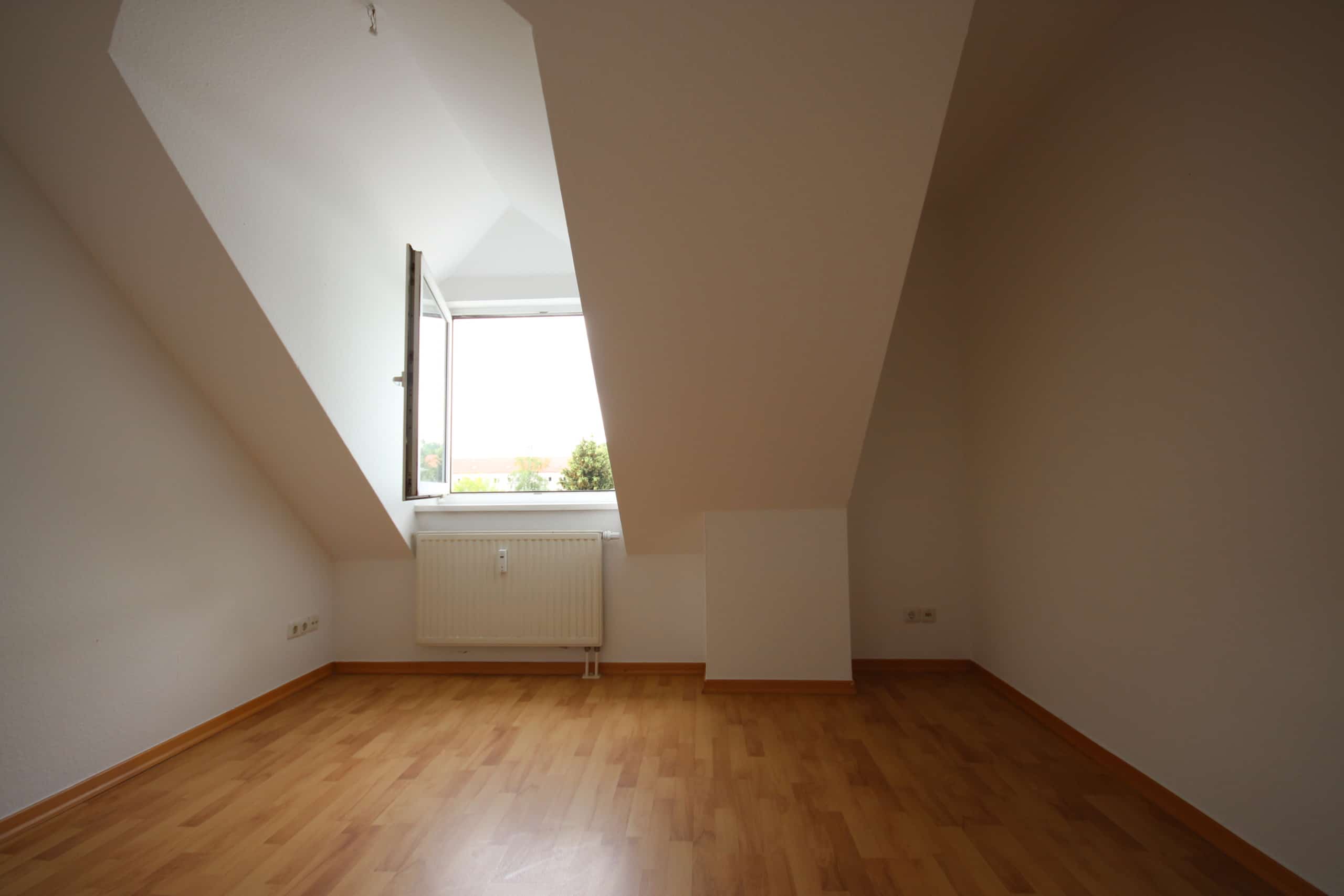 Leeres Dachgeschosszimmer mit schräger Decke offenem Dachfenster weißem Heizkörper und hellem Holz-Parkett