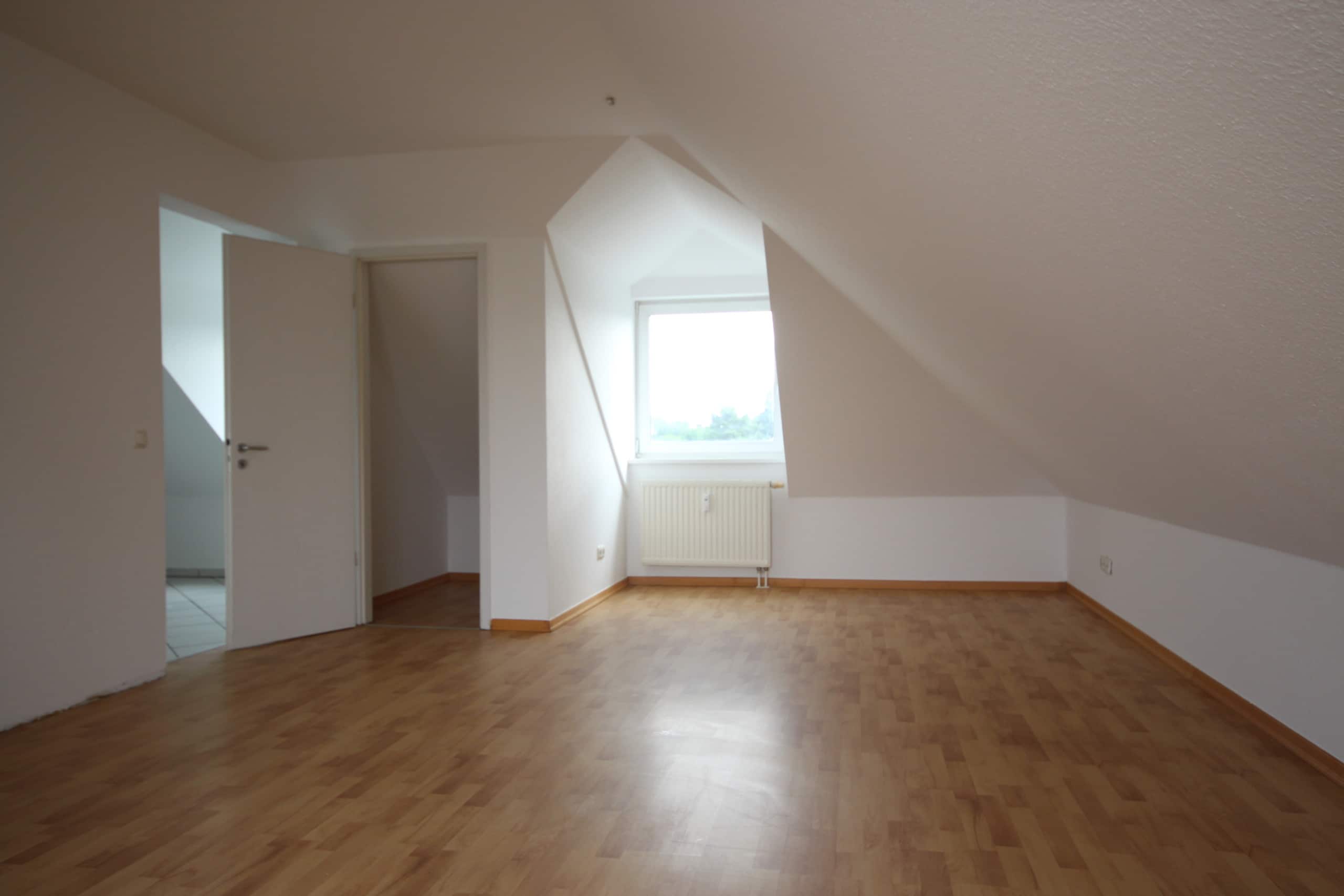 Dachgeschosswohnung innenansicht mit Dachschräge, hellem Laminatboden, weißen Wänden und Fenster mit Heizkörper