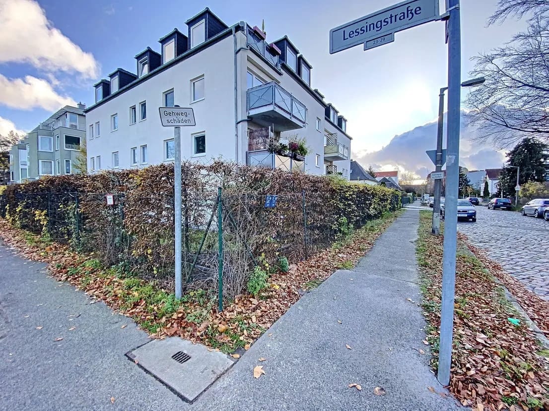 Straßenecke mit mehrgeschossigem Wohnhaus mit Putzfassade Balkonen und Heckeneinfriedung aus bodennaher Perspektive