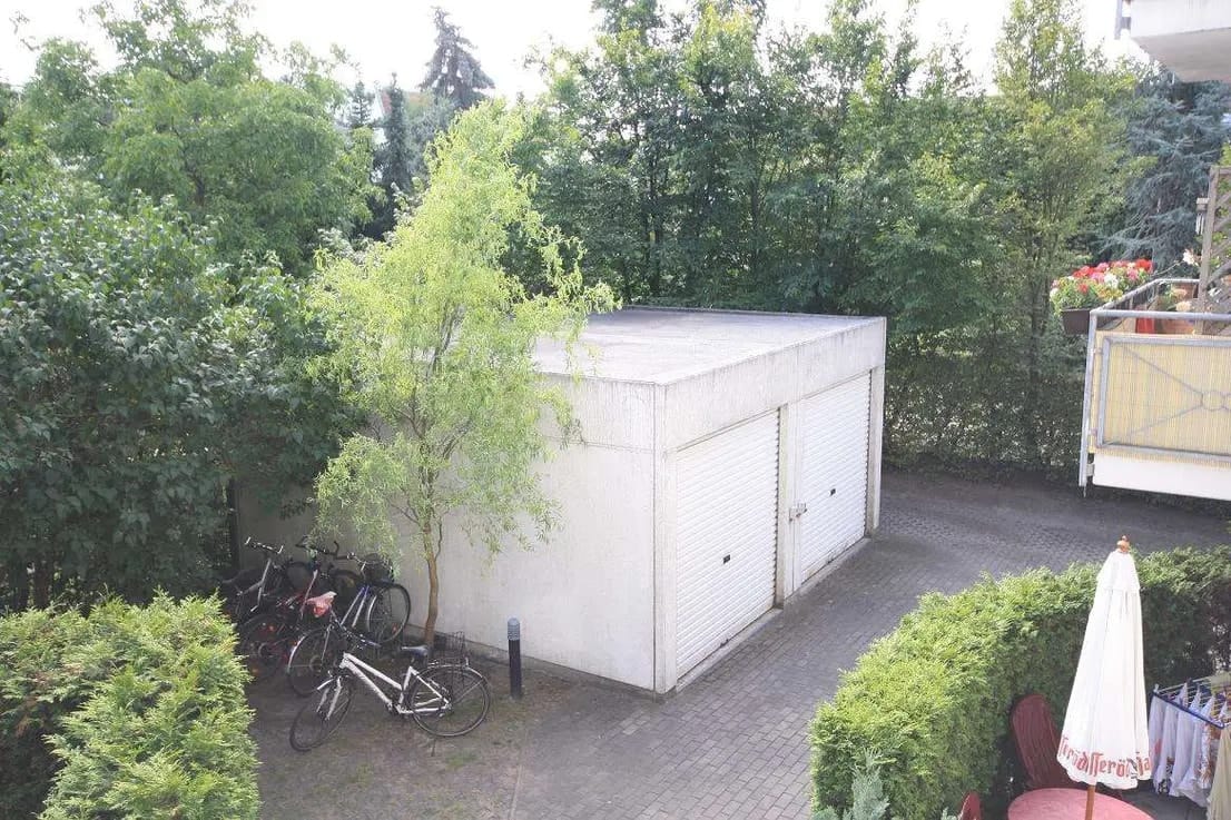 Vogelperspektive auf freistehende Doppelgarage mit Flachdach auf gepflastertem Hof umgeben von Büschen und Fahrrädern