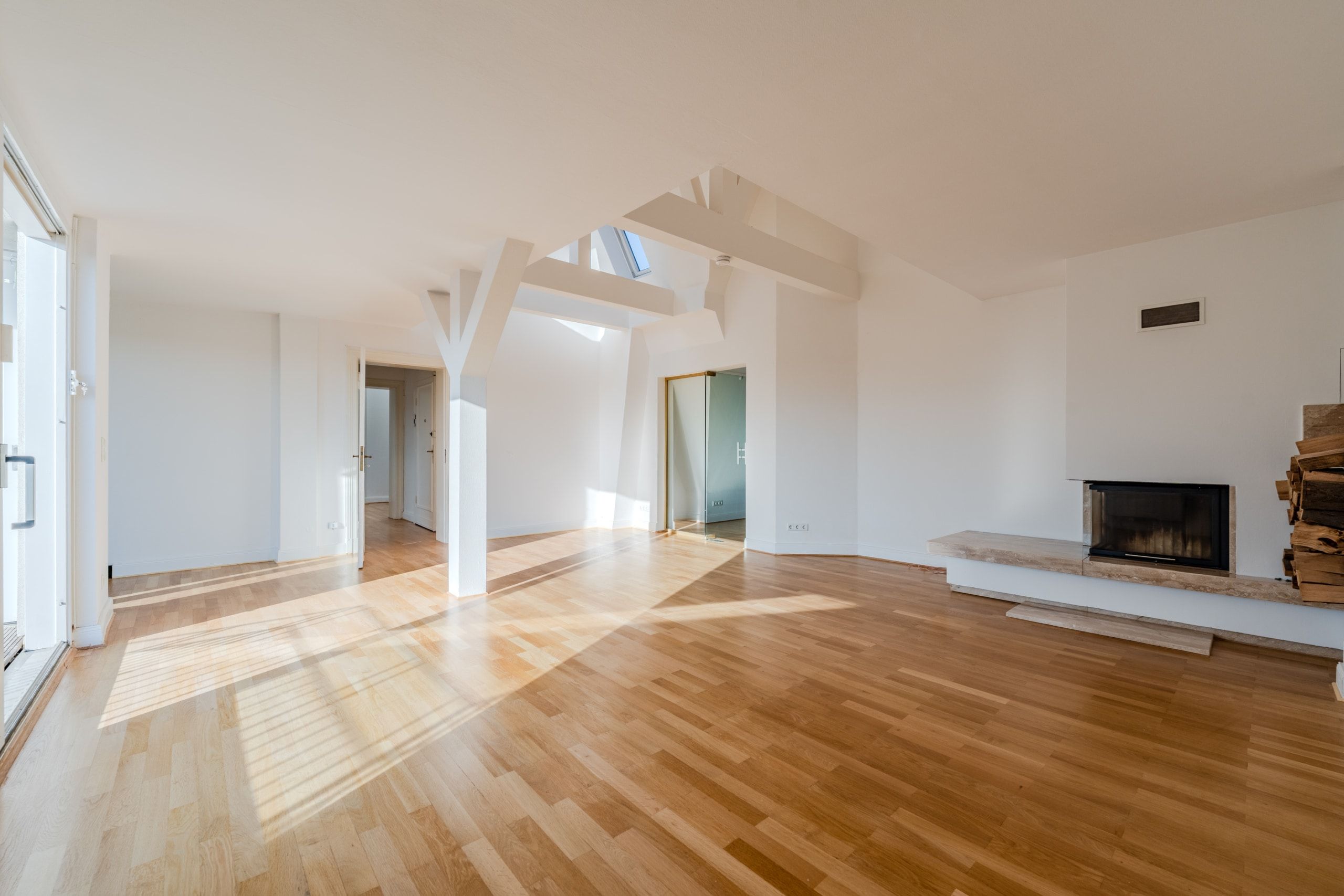 Interno di un luminoso appartamento mansardato con zona giorno a pianta aperta, travi a vista, pavimento in parquet e camino