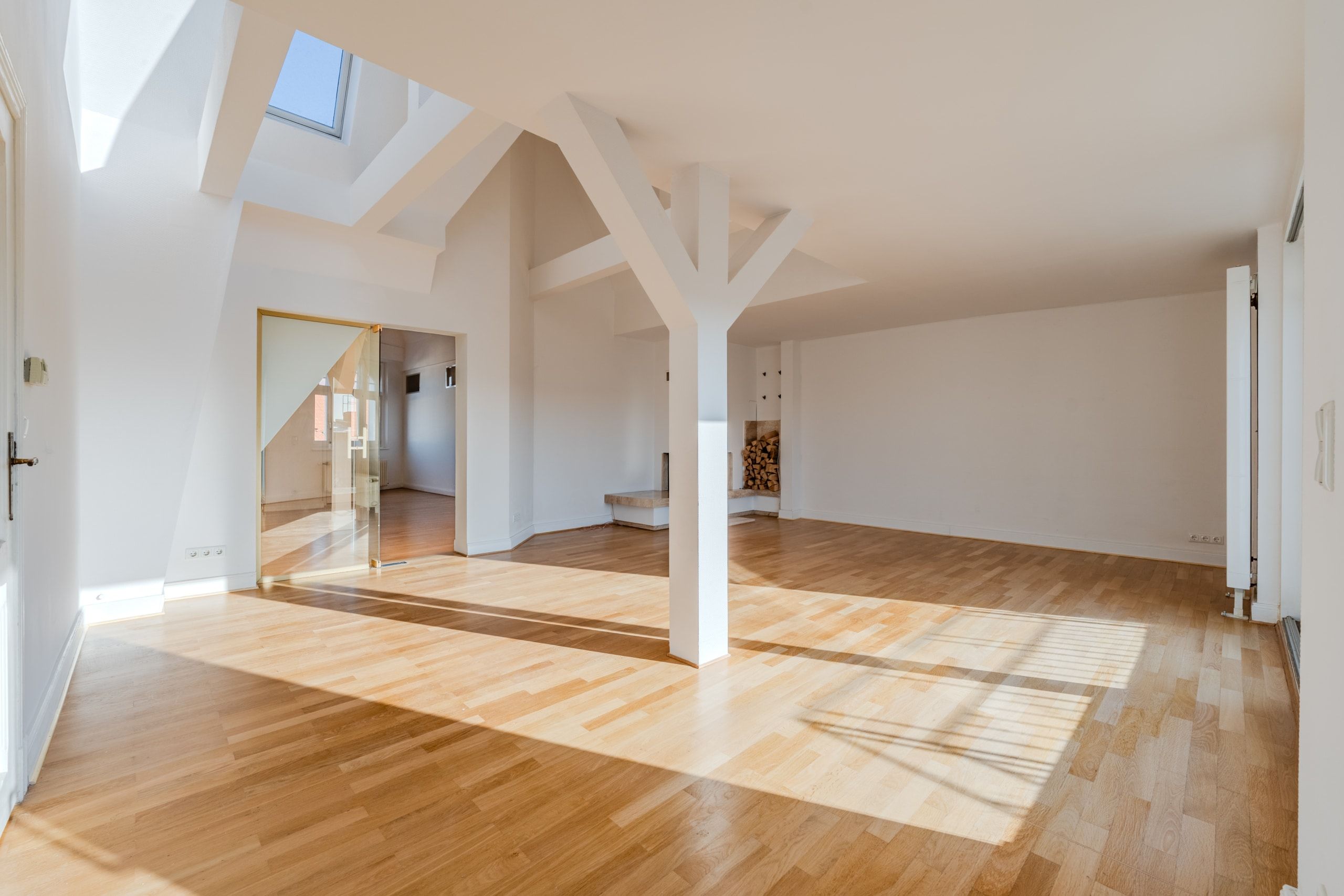 Soggiorno a vista nella mansarda con travi a vista bianche, pavimento in parquet, lucernari e porta scorrevole in vetro