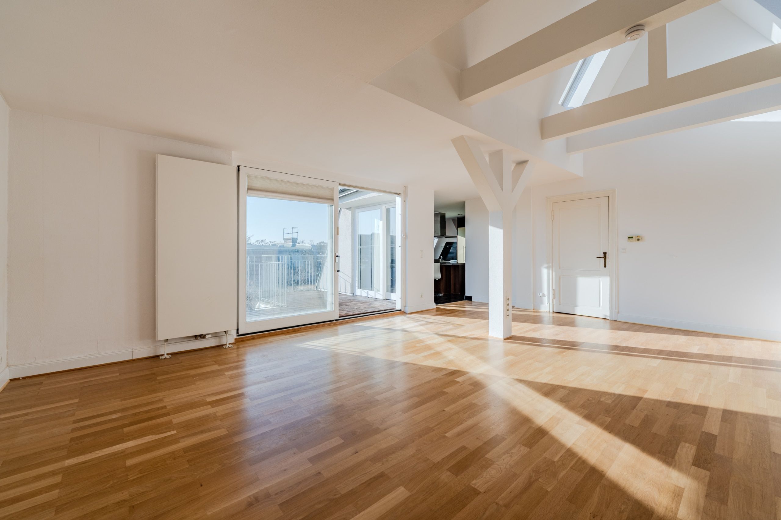 Attico: zona giorno vista da un angolo, con pavimento in parquet, travi a vista e accesso al balcone tramite porta scorrevole