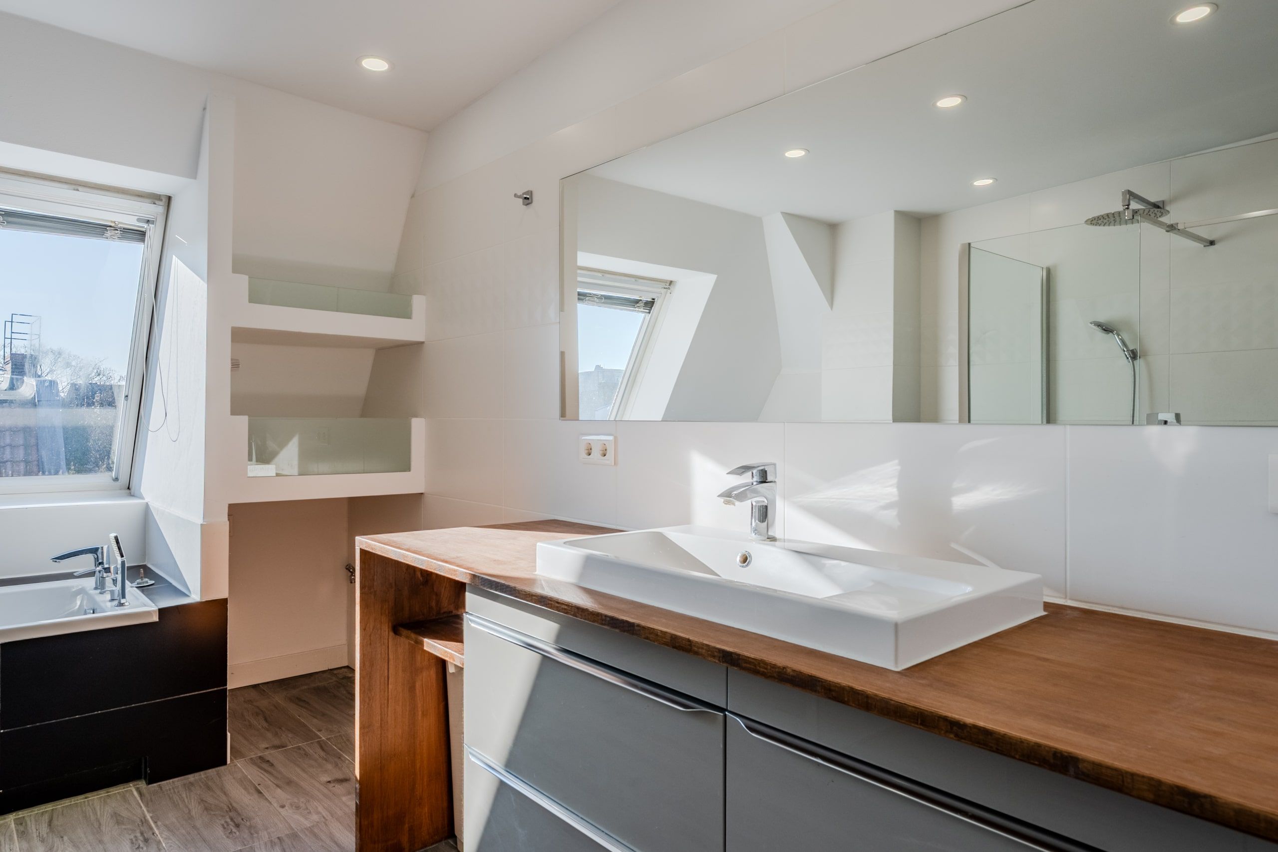 Vista interna di un moderno bagno mansardato con vasca da bagno indipendente, ampio specchio e lavabo incassato in un piano di lavoro in legno