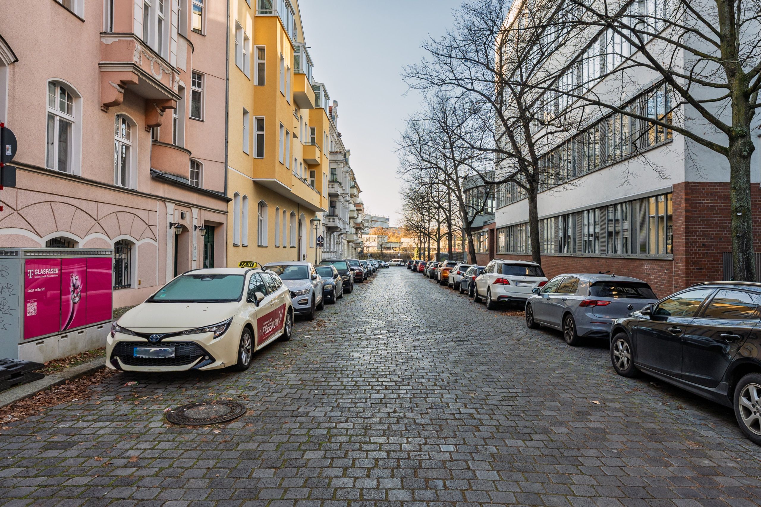 Vista della strada con edifici storici dalle facciate intonacate dai colori vivaci e dai balconi, lungo una strada acciottolata con auto parcheggiate