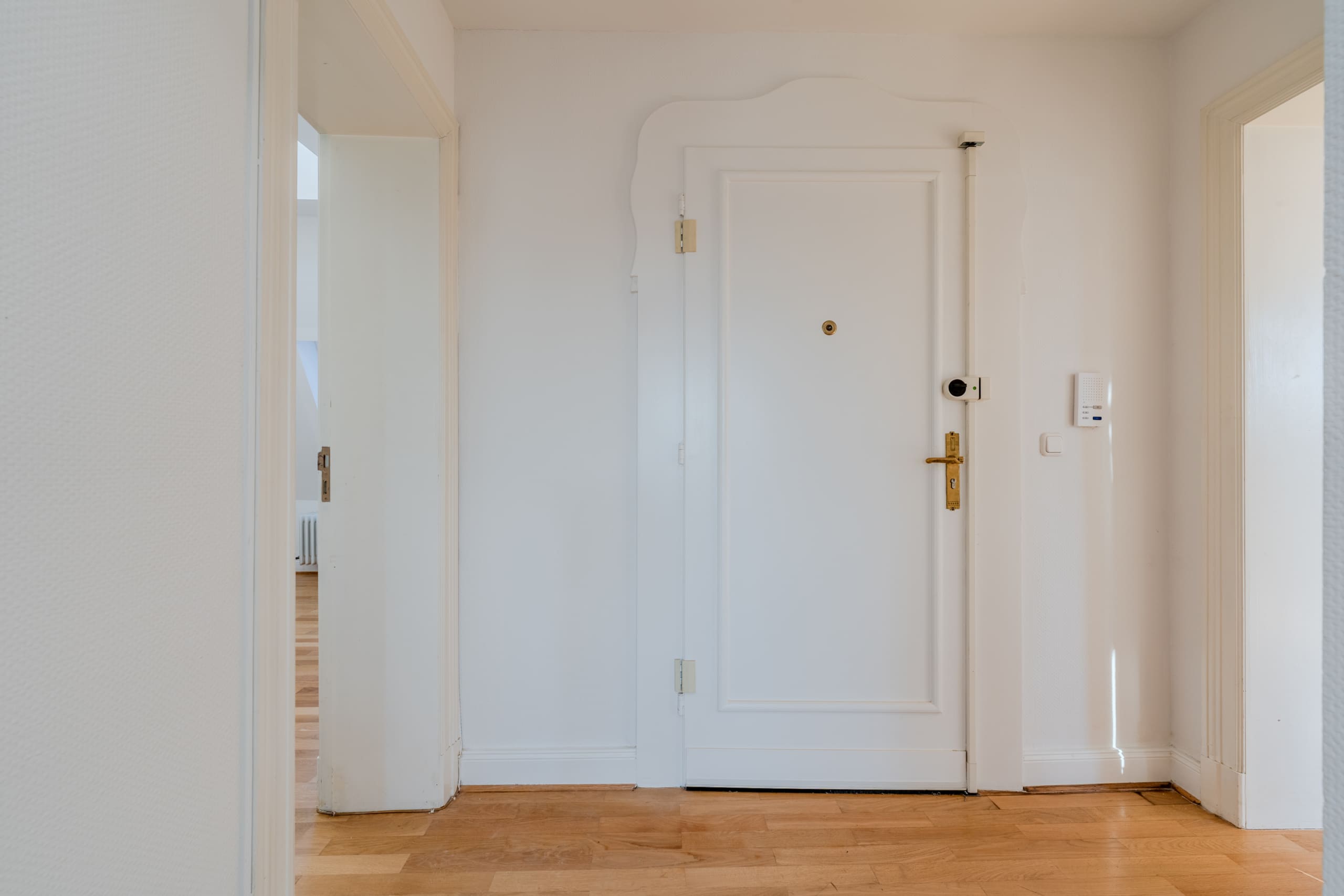 Corridoio interno di un appartamento con porta d'ingresso bianca, pavimento in parquet e due porte di stanze aperte