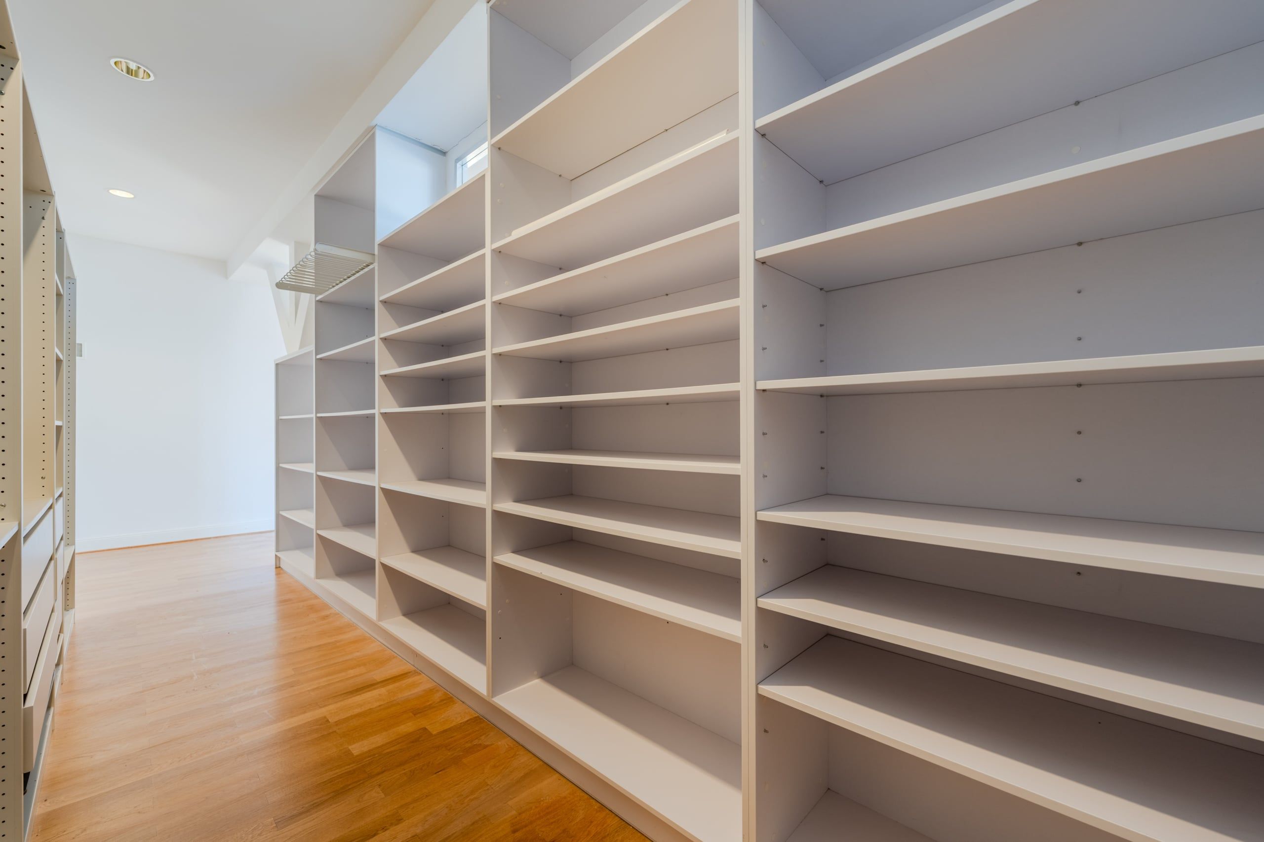 Camera armadio con ripiani bianchi e soffitto spiovente su pavimento in parquet, vista laterale