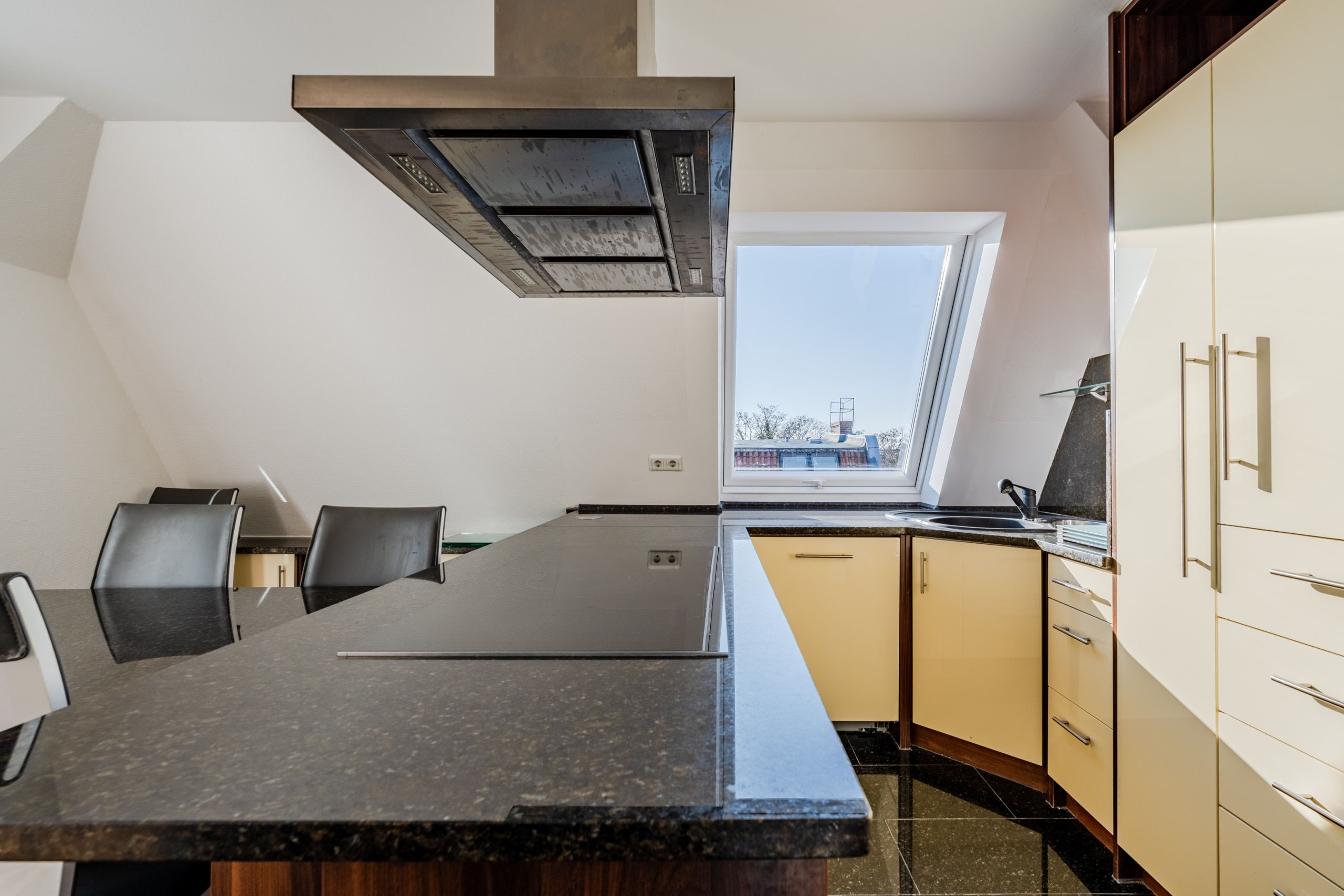 Cucina a vista nell'attico con isola di cottura e piano in granito nero sotto la finestra da mansarda