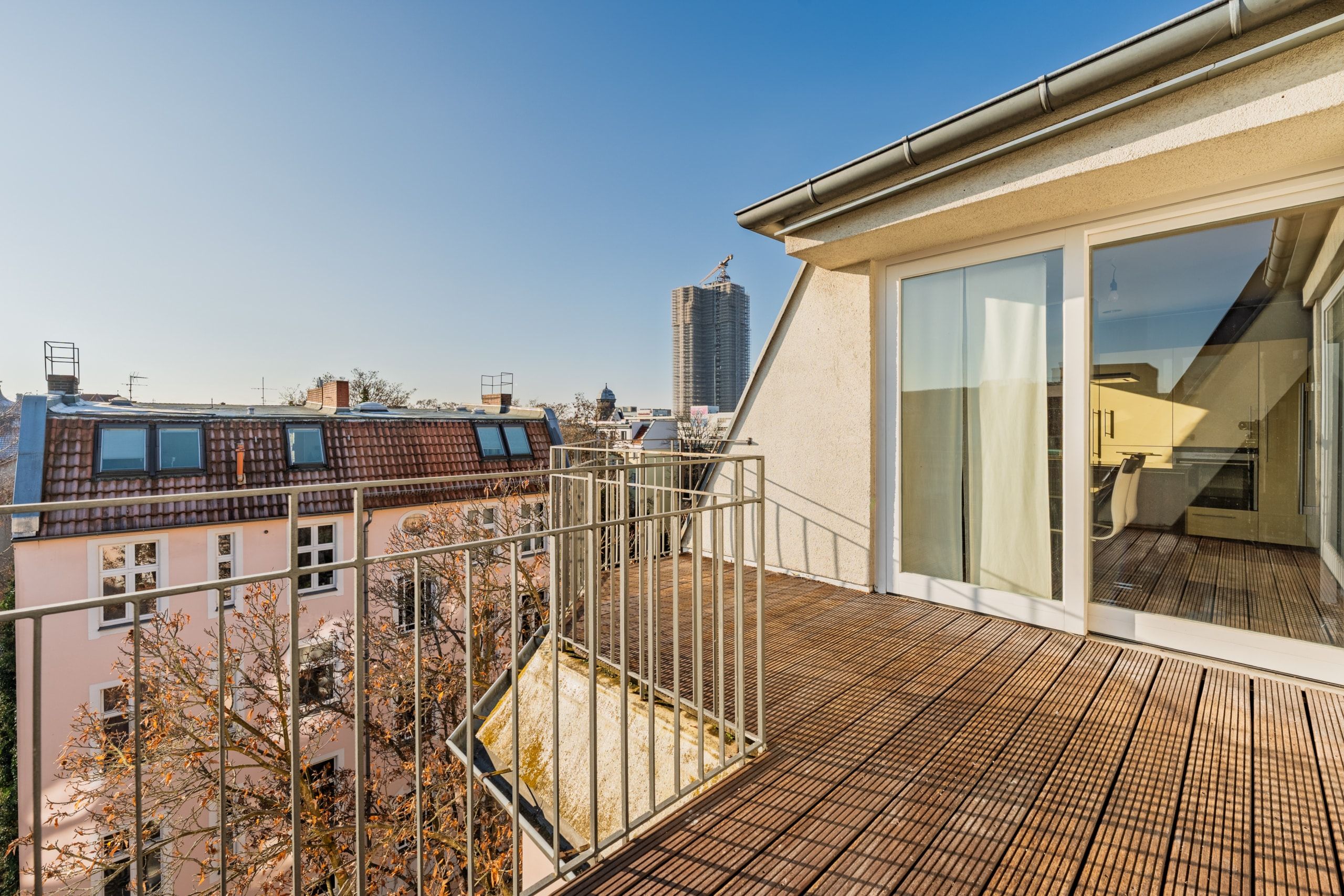 Vista dalla terrazza sul tetto di un attico: pavimento in parquet, ringhiera metallica perimetrale e porte scorrevoli in vetro a tutta altezza