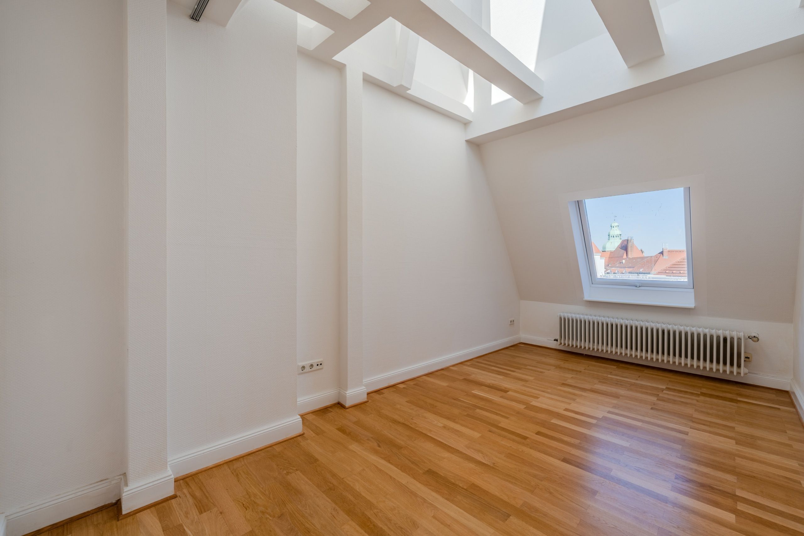Vista interna di una stanza vuota nella mansarda con parquet in legno, lucernario, travi a vista e radiatori a parete