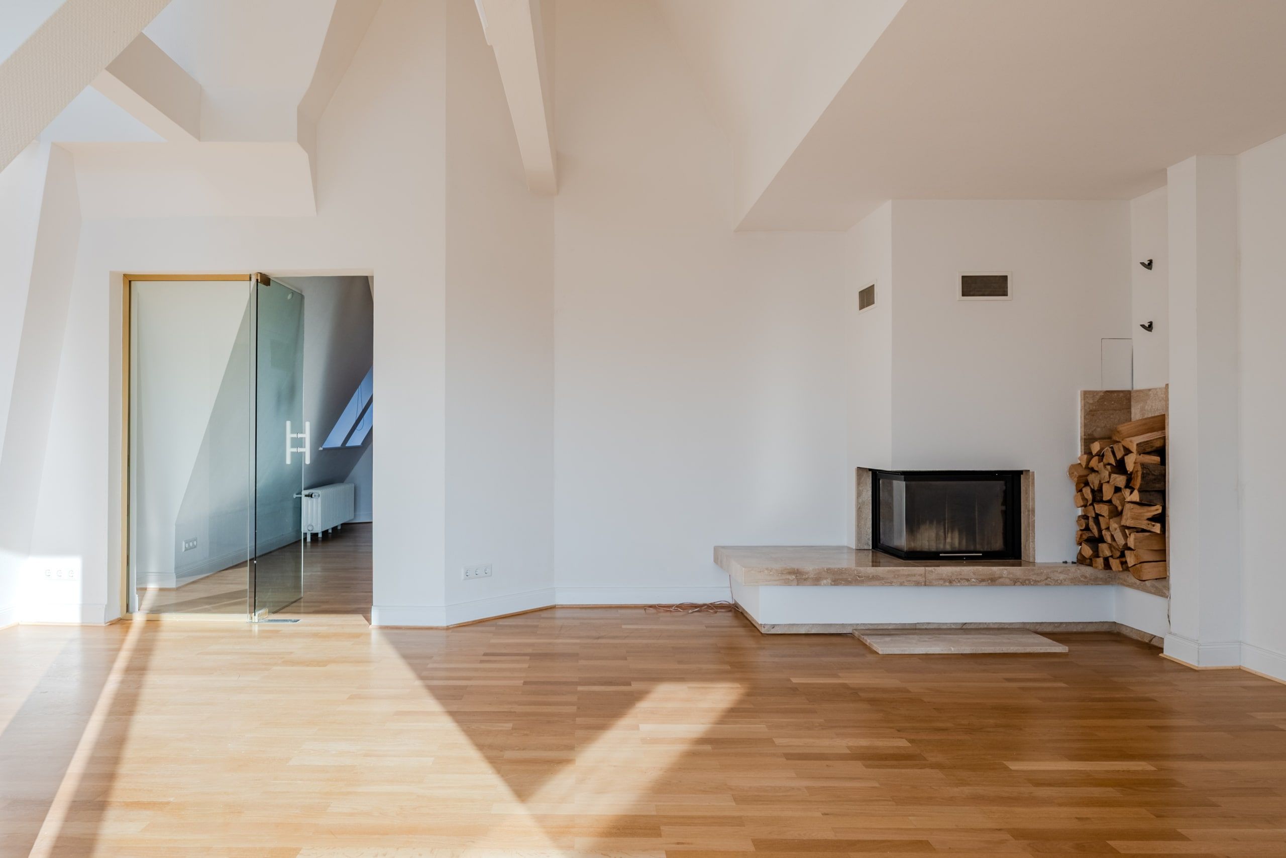 Interno di un luminoso loft mansardato con pavimento in parquet, porta scorrevole in vetro e camino con vano per la legna