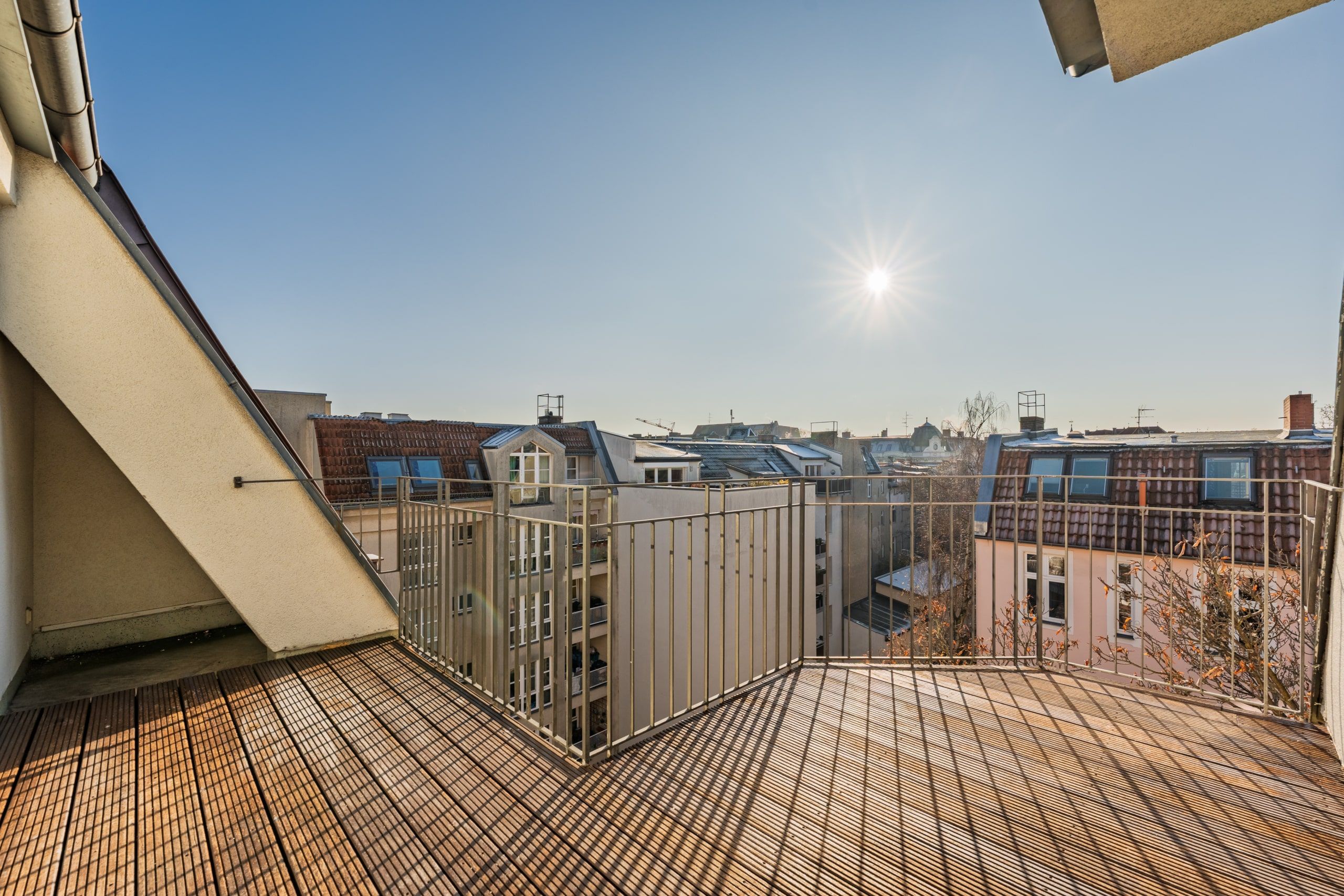 Terrazza sul tetto con pavimentazione in legno e ringhiera metallica sul lato anteriore, con vista sui tetti della città circostante