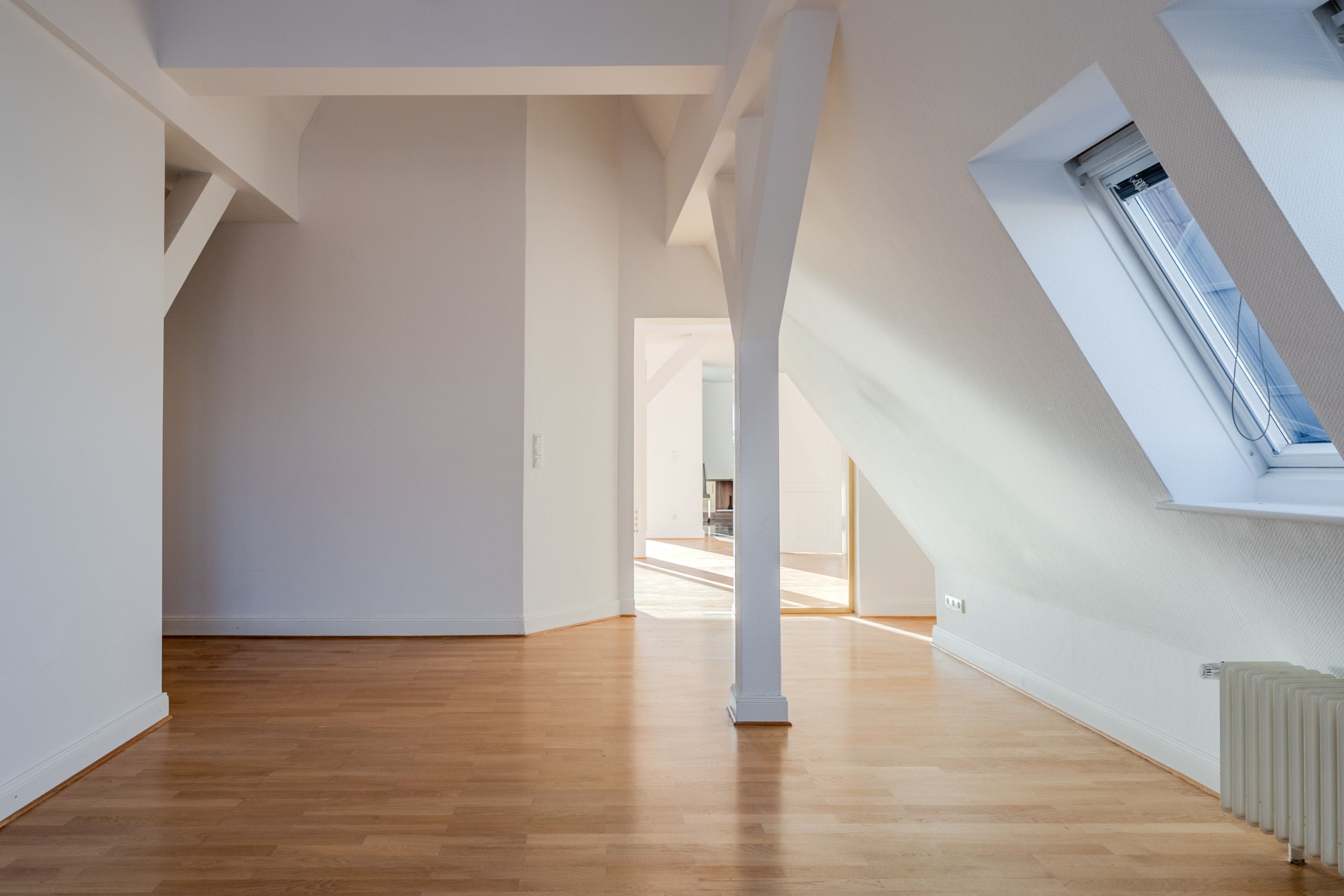 Appartamento mansardato a pianta aperta visto dall'interno, con soffitto spiovente, pilastro centrale, pavimenti in parquet e lucernari