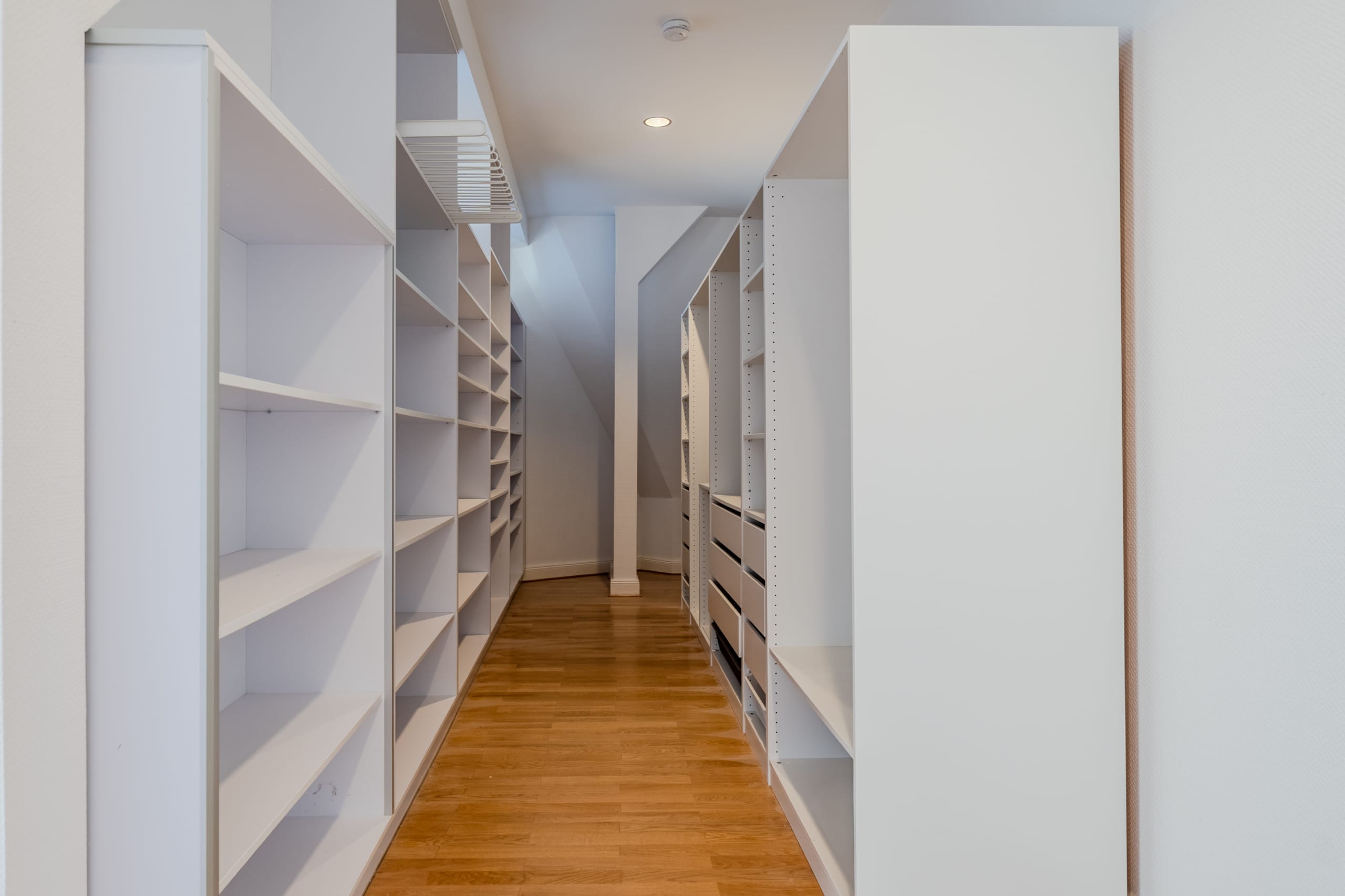 Vista interna della cabina armadio con ripiani bianchi su entrambi i lati e pavimento in parquet chiaro, vista dal corridoio