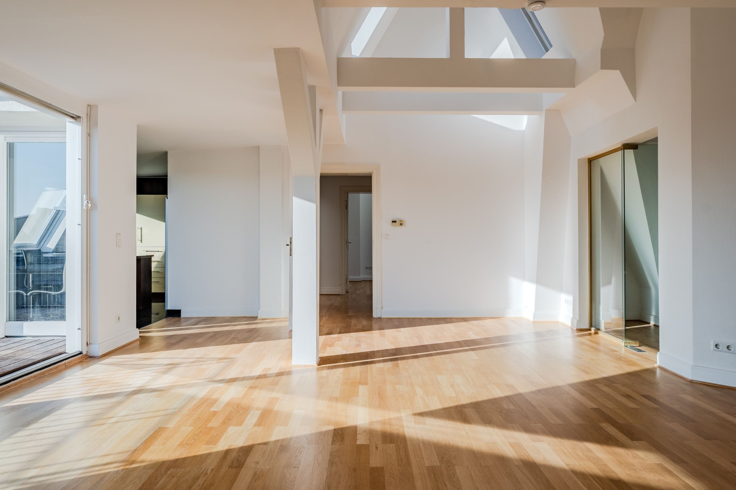 Interno di un moderno appartamento mansardato con zona giorno a pianta aperta, travi a vista, pavimento in parquet, lucernari e accesso al balcone