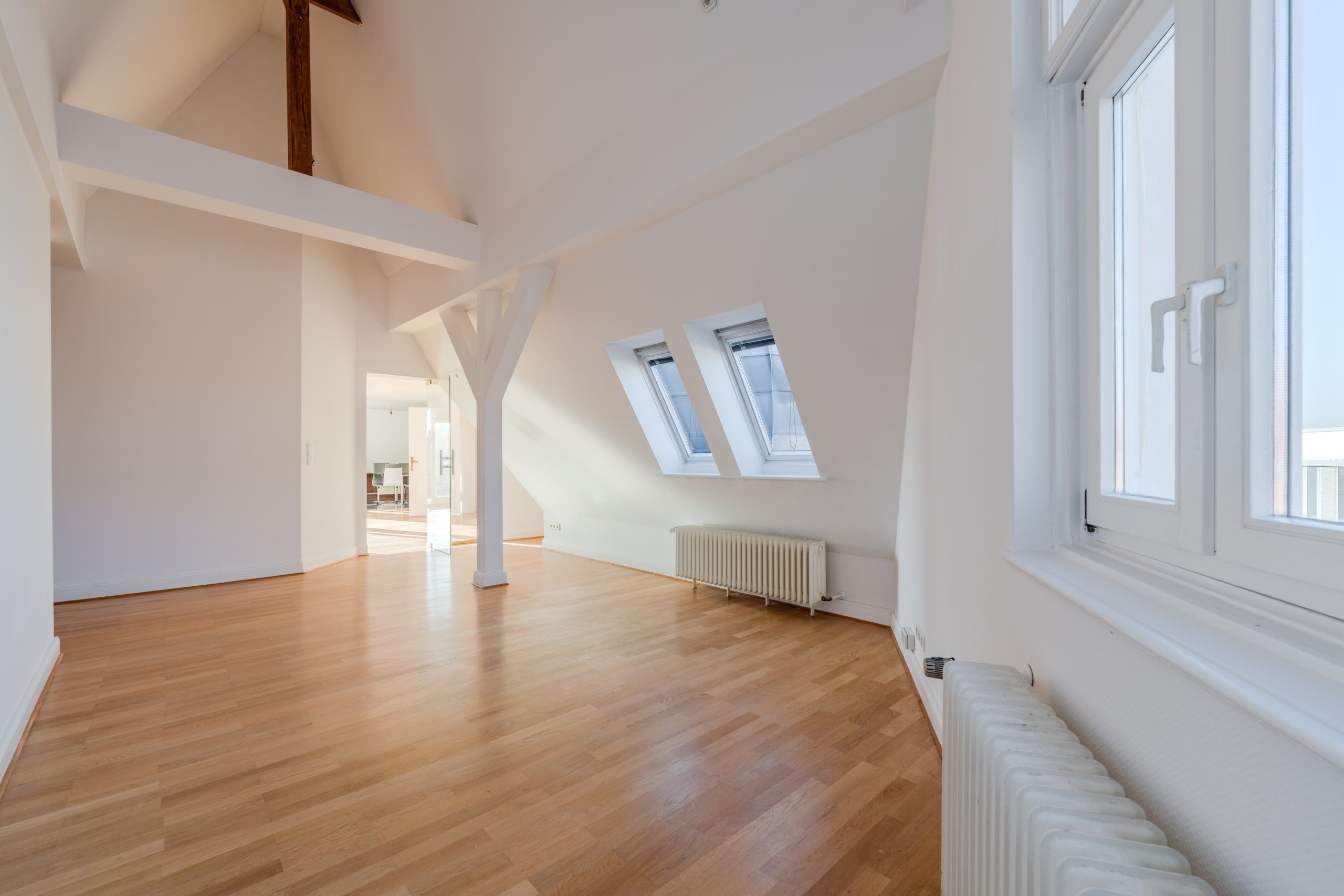 Interno di un luminoso appartamento mansardato con pianta aperta, pavimento in parquet, travi a vista e due lucernari