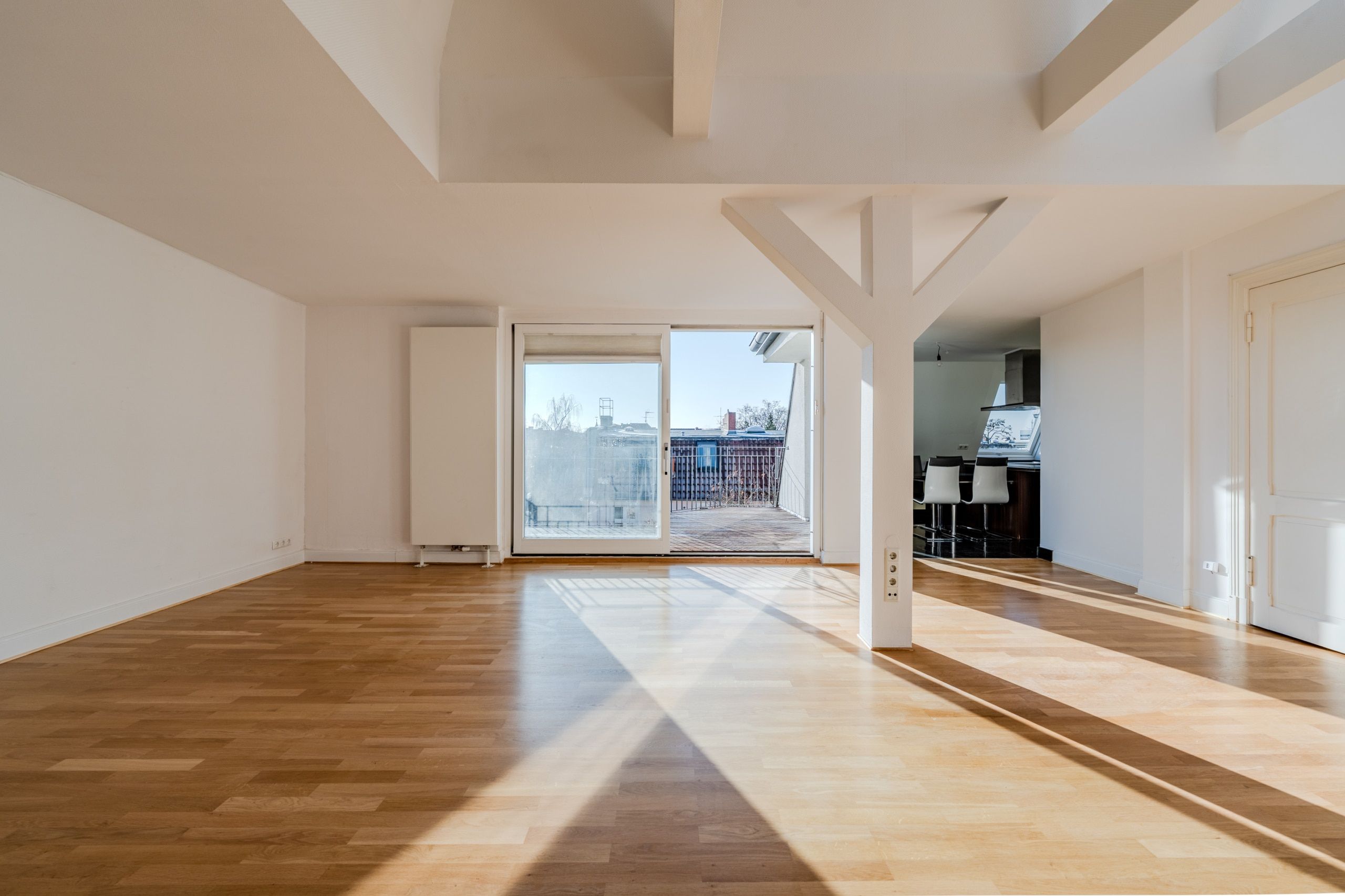 Interno dell'appartamento mansardato con vista sulla terrazza in legno, travi a vista bianche e pavimento in parquet chiaro