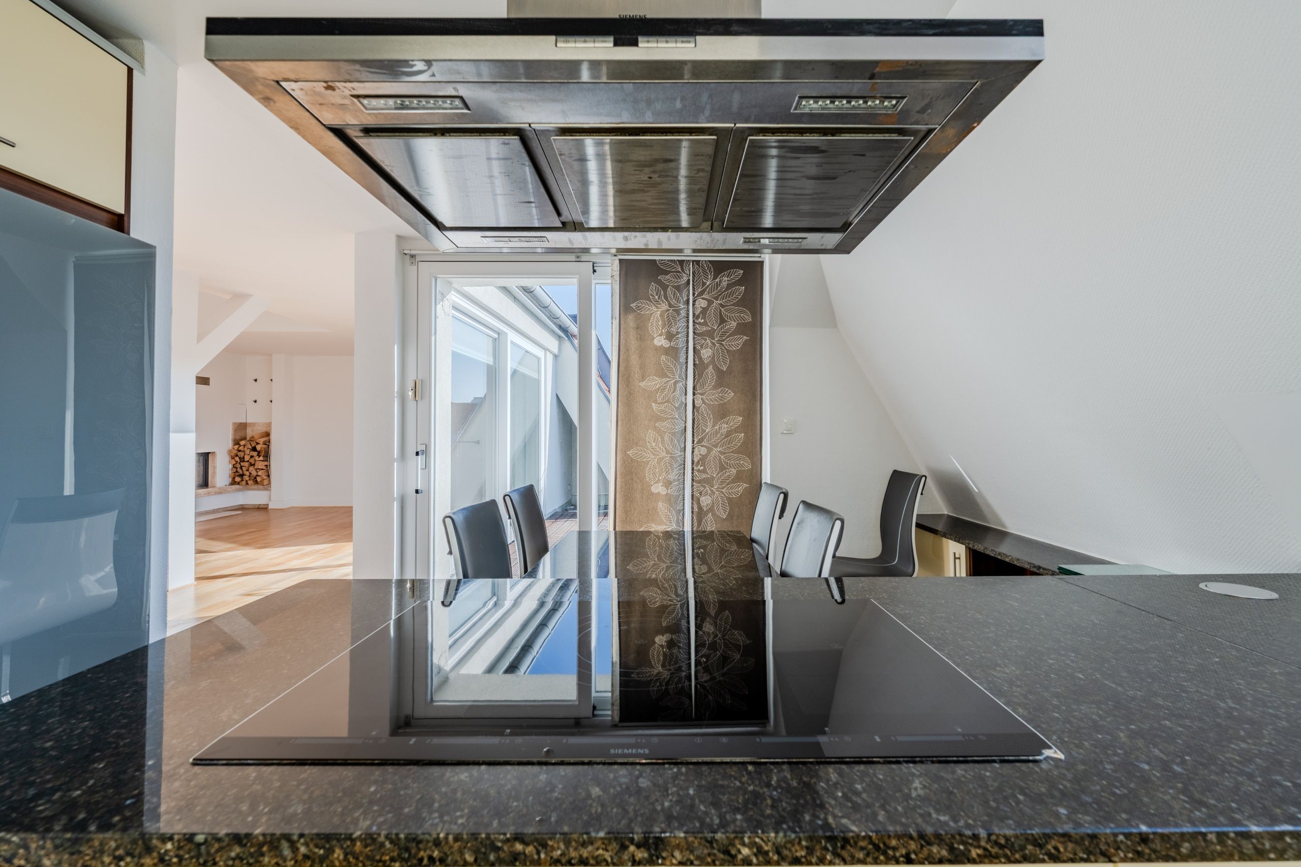 Vista dalla moderna isola cucina sulla zona giorno aperta dell'attico, con piano cottura a induzione, cappa aspirante e porta finestra