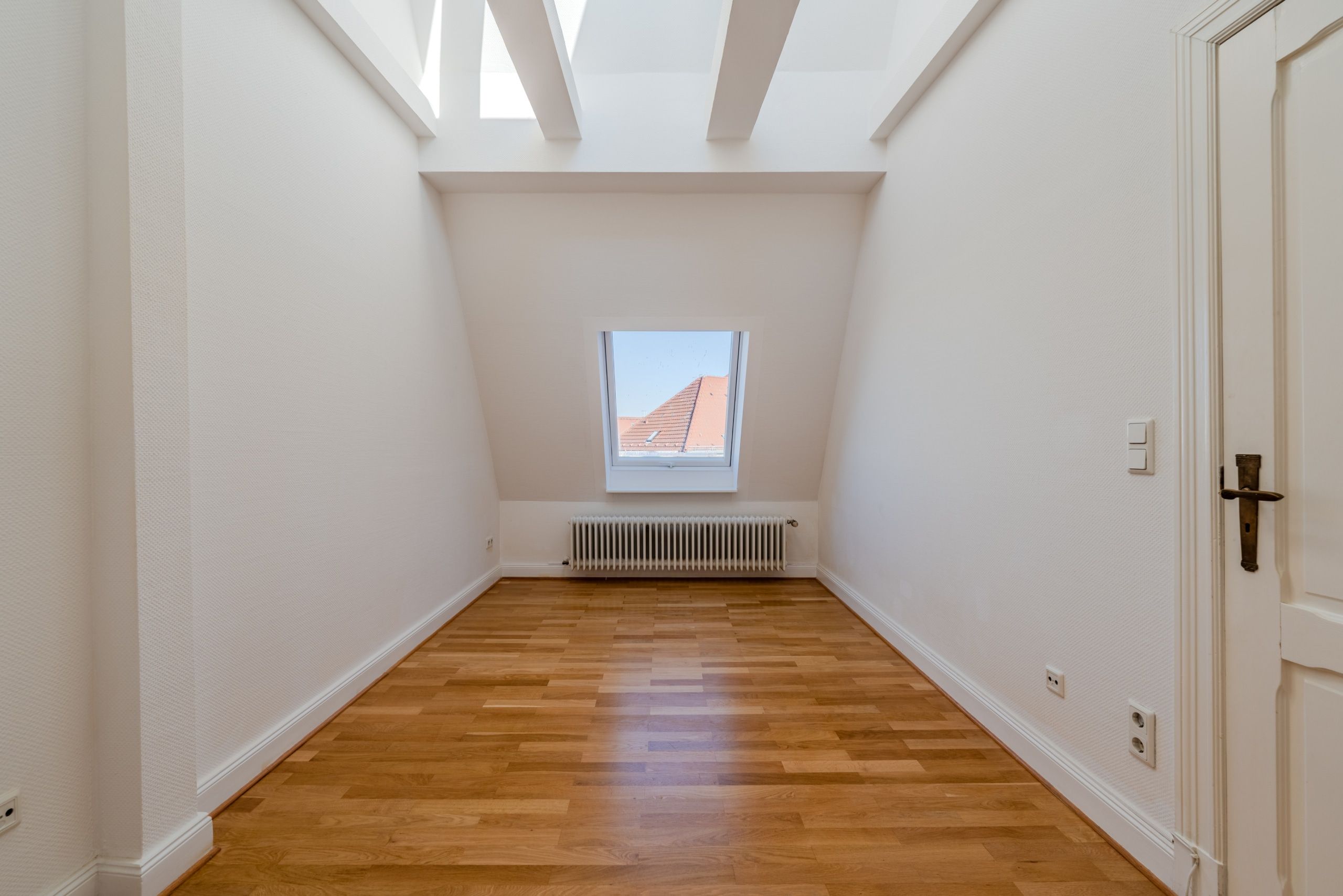 Camera mansardata libera con pavimento in parquet, finestra da tetto e radiatore