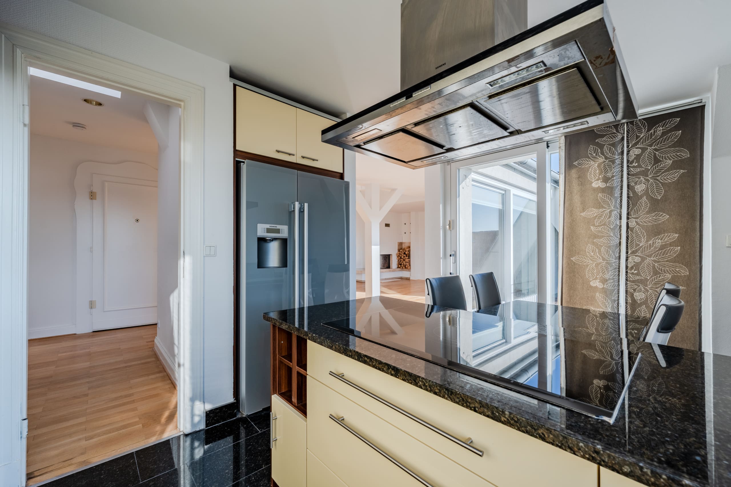 Cucina a vista con isola, piano cottura a induzione, cappa in acciaio inossidabile, frigorifero capiente e vista sulla zona giorno