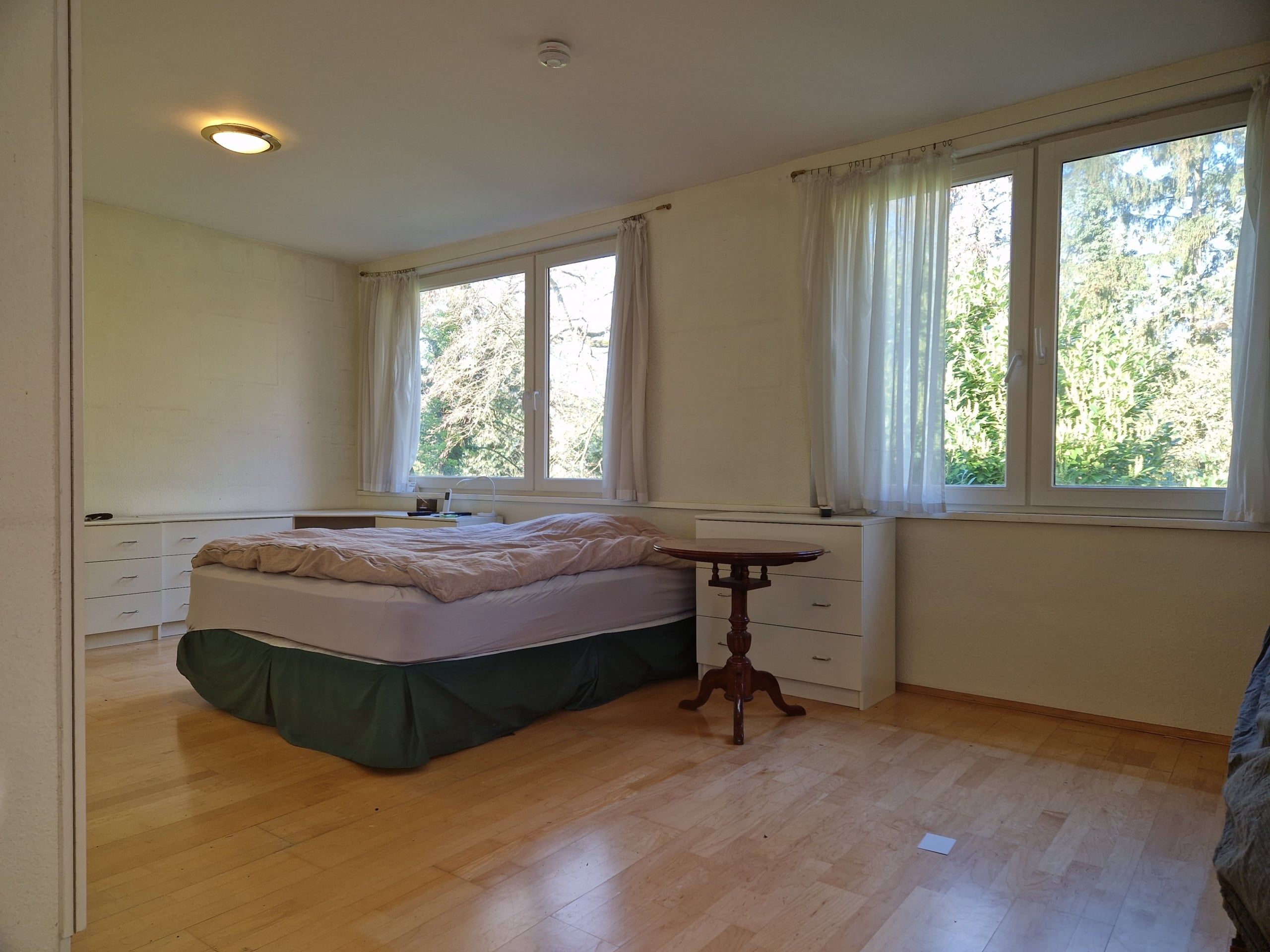 Innenansicht Schlafzimmer aus Flurperspektive mit Doppelbett großem Fenster Gardinen Kommode Parkettboden