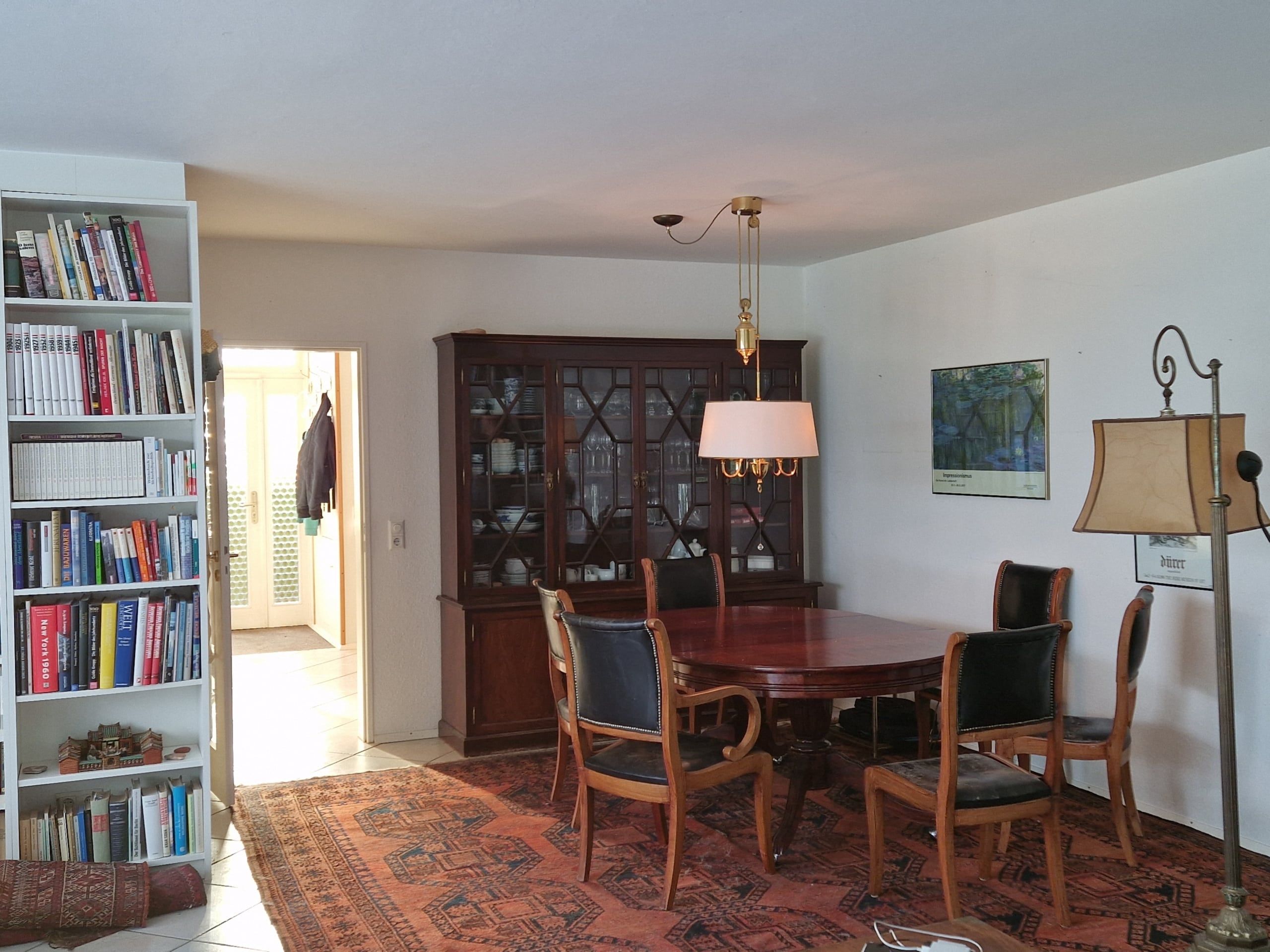 Blick in Esszimmer eines Einfamilienhauses aus offener Diele mit Holztisch, Bücherschrank, Glasvitrine und Orientteppich