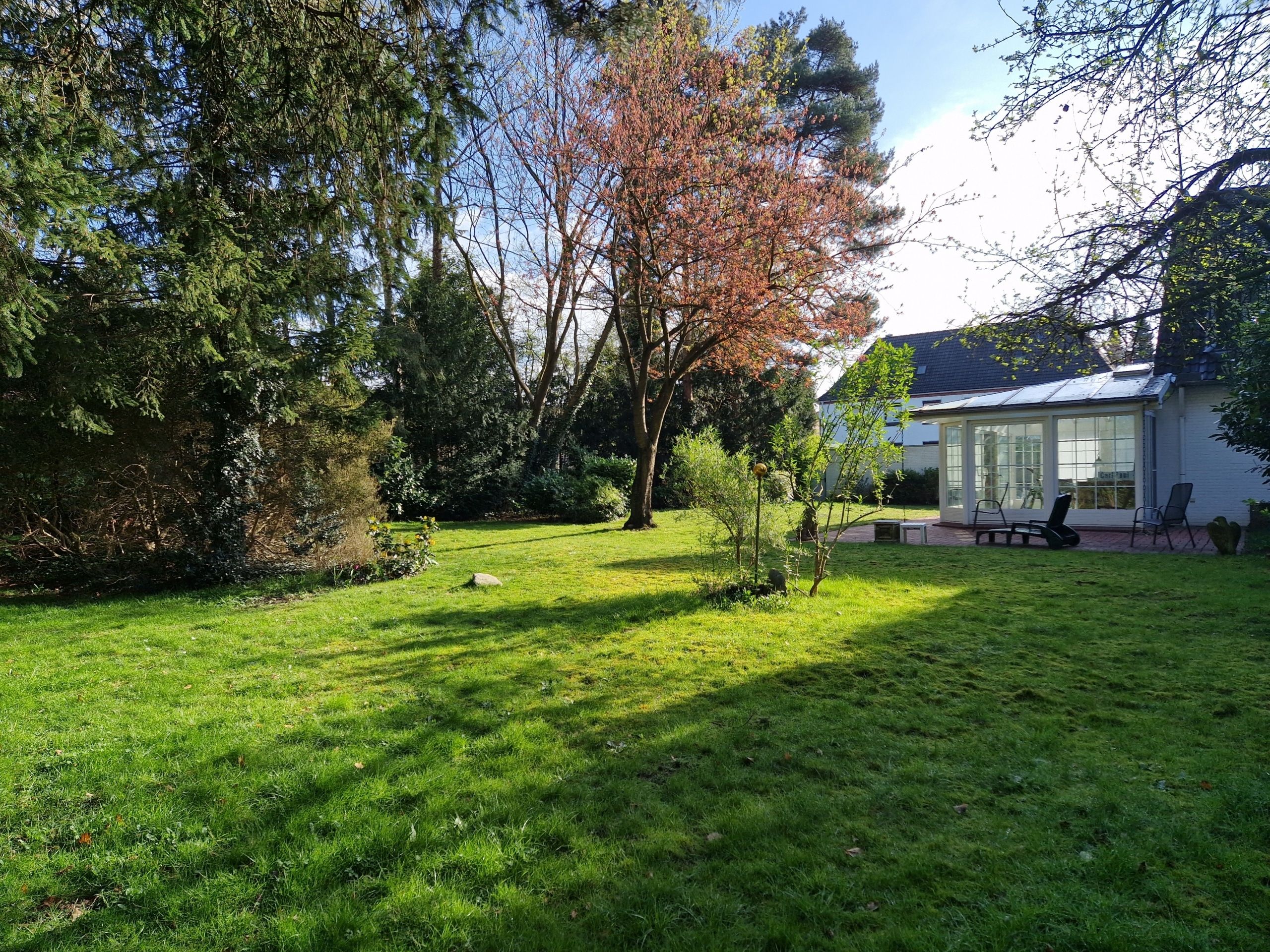 Einfamilienhaus mit verglastem Wintergarten im großen Garten mit Rasen und Bäumen aus niedriger Perspektive