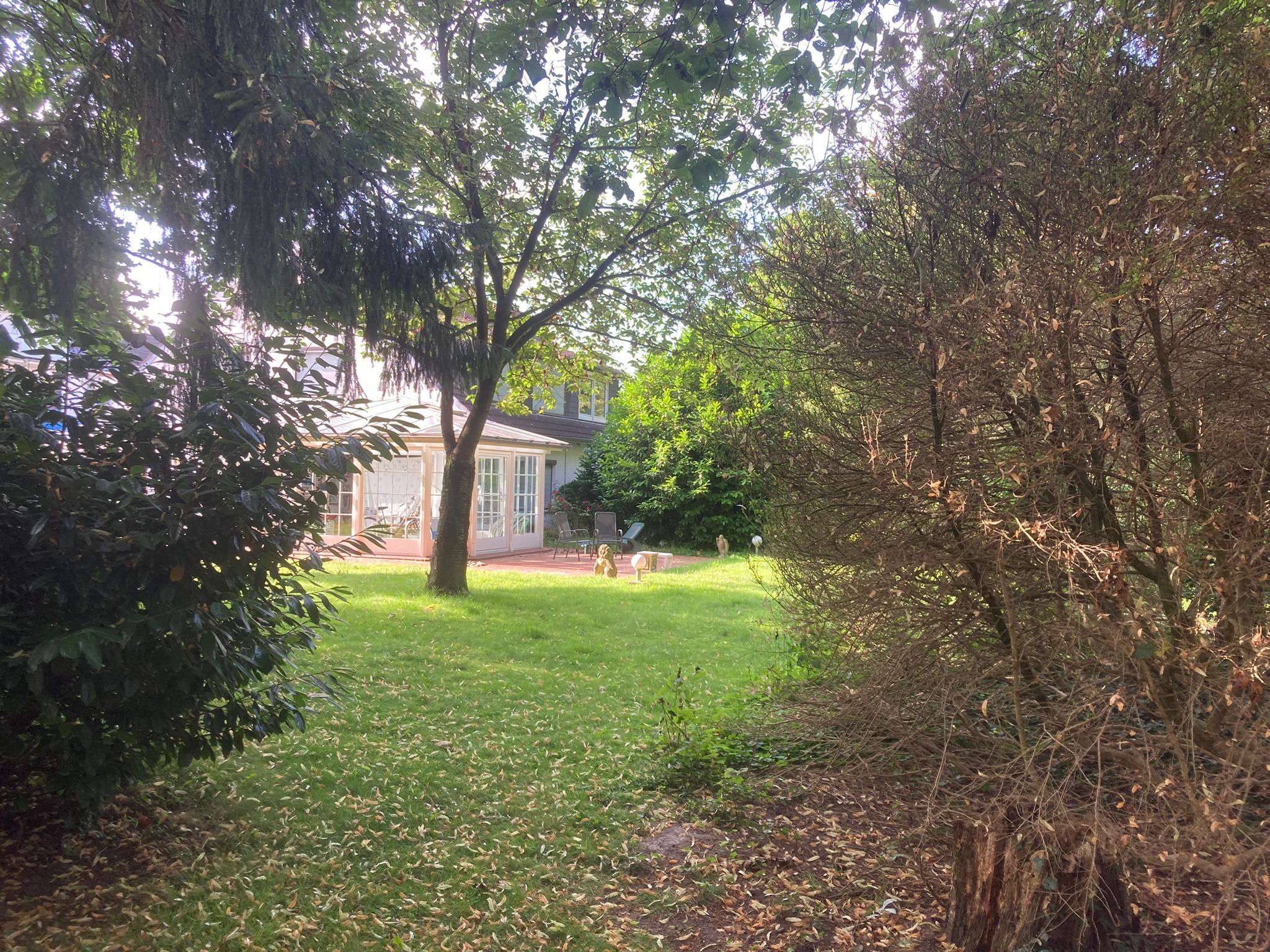 Gartenblick auf Einfamilienhaus mit verglastem Wintergarten und Terrasse