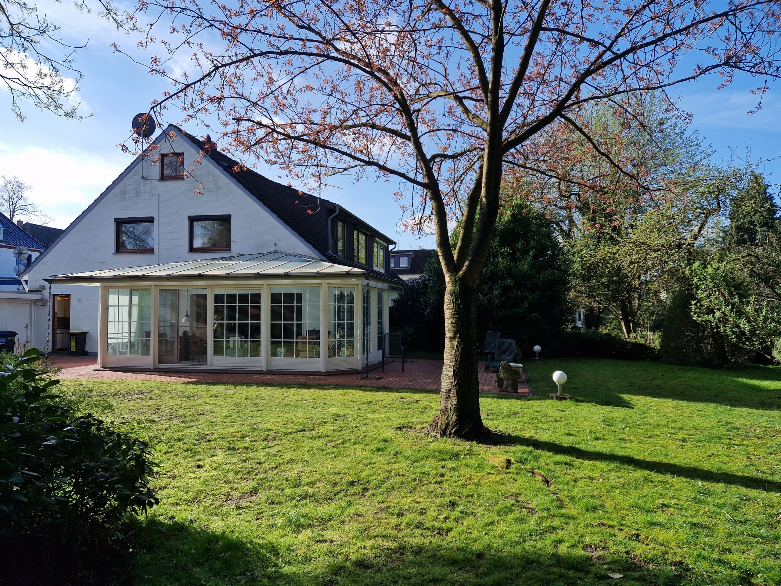 Gartenansicht eines weißen Einfamilienhauses mit Glaswintergarten seitlicher Giebelfassade und großem Rasenbereich