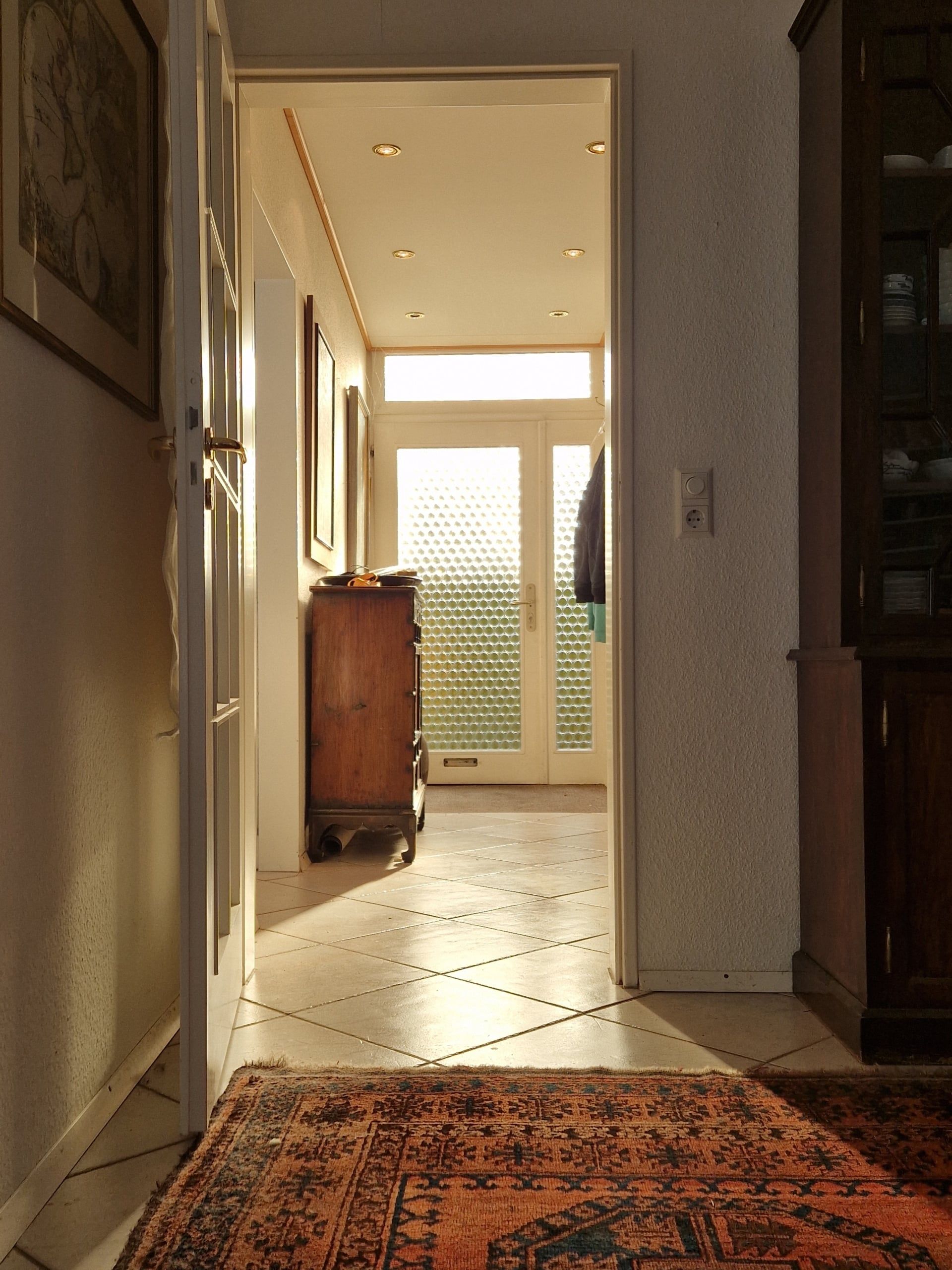 Blick in den Flur einer Wohnung mit Fliesenboden orientalischem Teppich Holzkommode und satinierten Glastüren