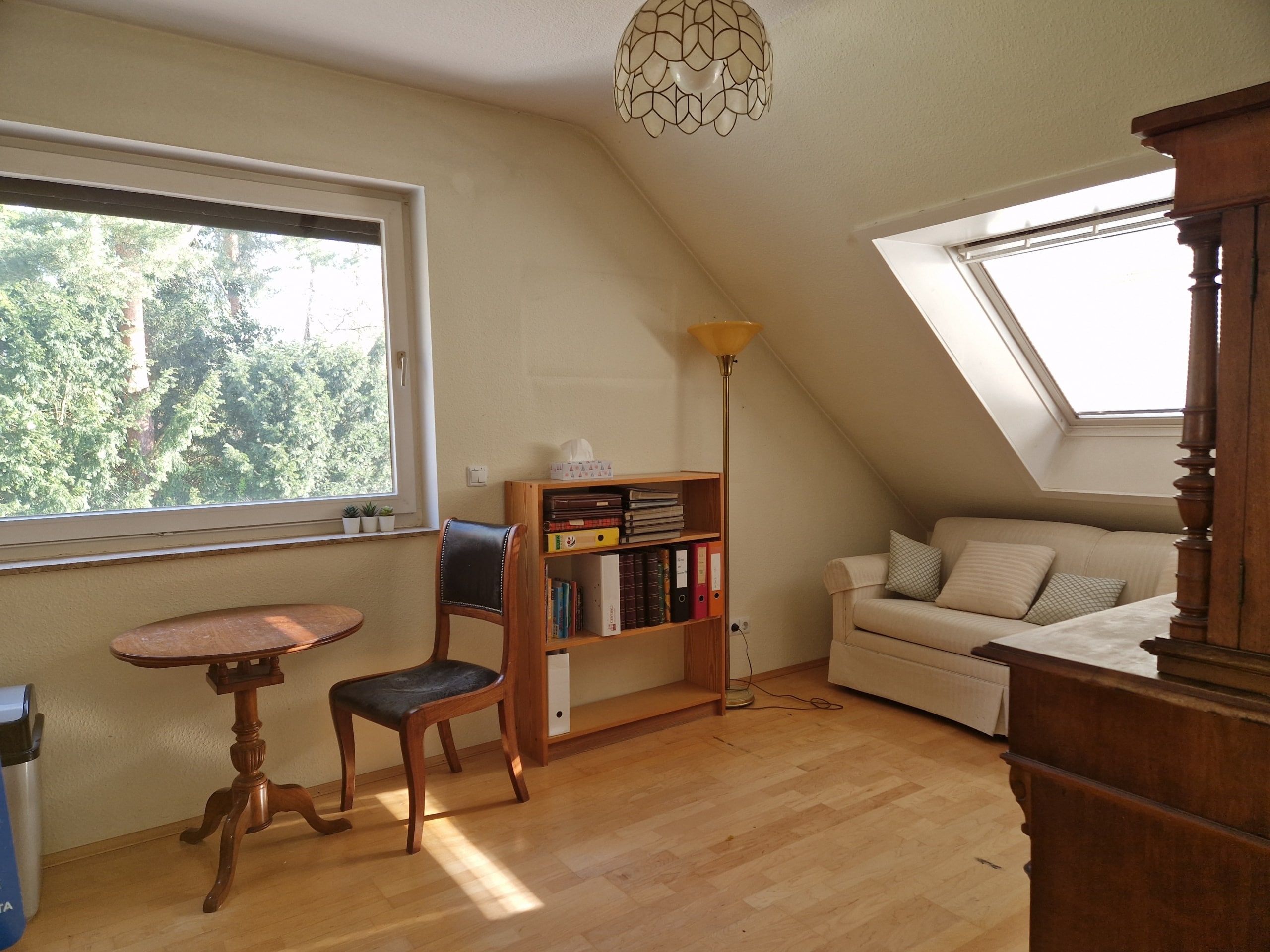Ausgebautes Dachgeschosszimmer mit Holzboden Sessel Beistelltisch Regal und Sofabereich unter Dachflächenfenster