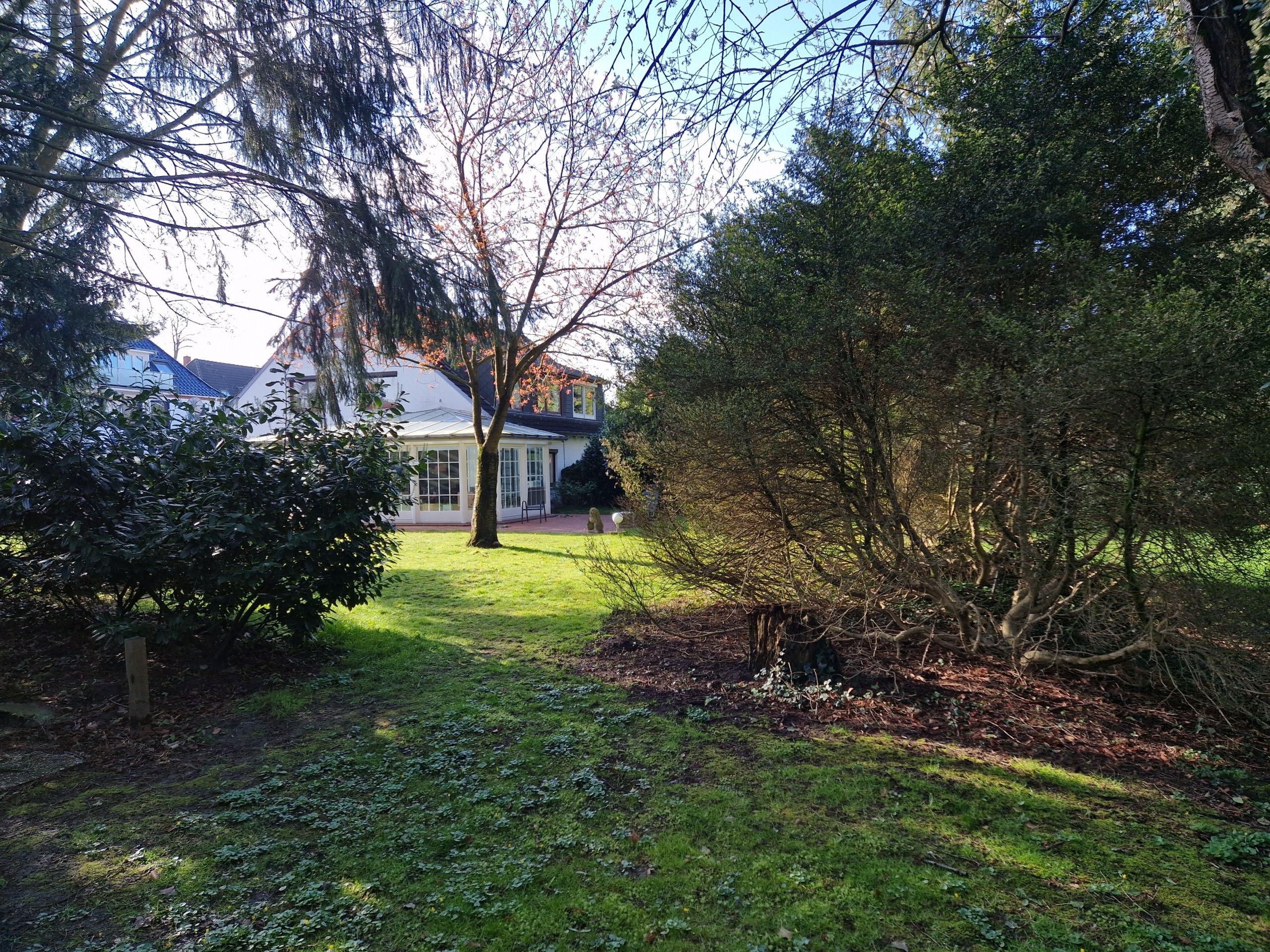 Gartenansicht eines Einfamilienhauses mit Wintergarten, gepflegtem Rasen und umstehenden Bäumen