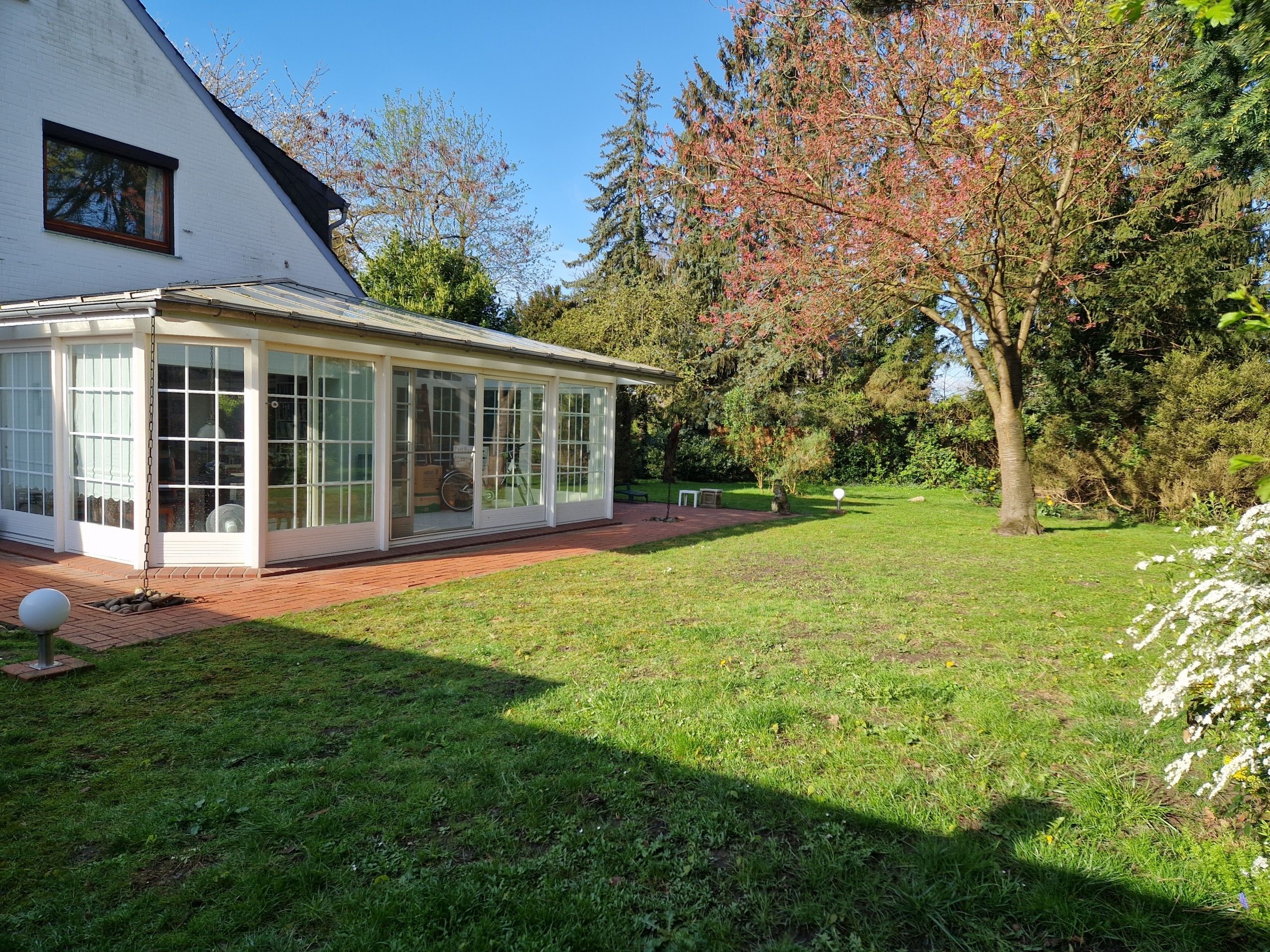 Einfamilienhaus mit verglastem Wintergarten in Seitenansicht und großzügigem Garten mit Rasen und Bäumen
