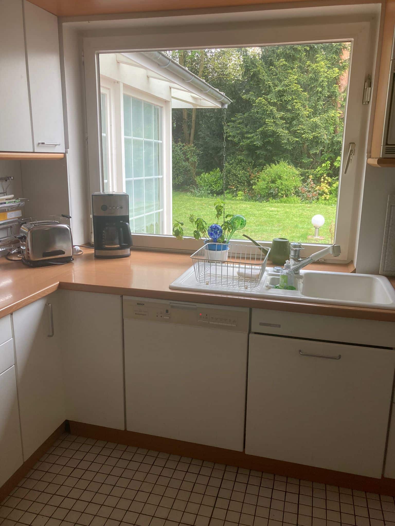 Blick in moderne Einbauküche mit Spüle, Geschirrspüler und Arbeitsfläche vor großem Fenster mit Gartenblick