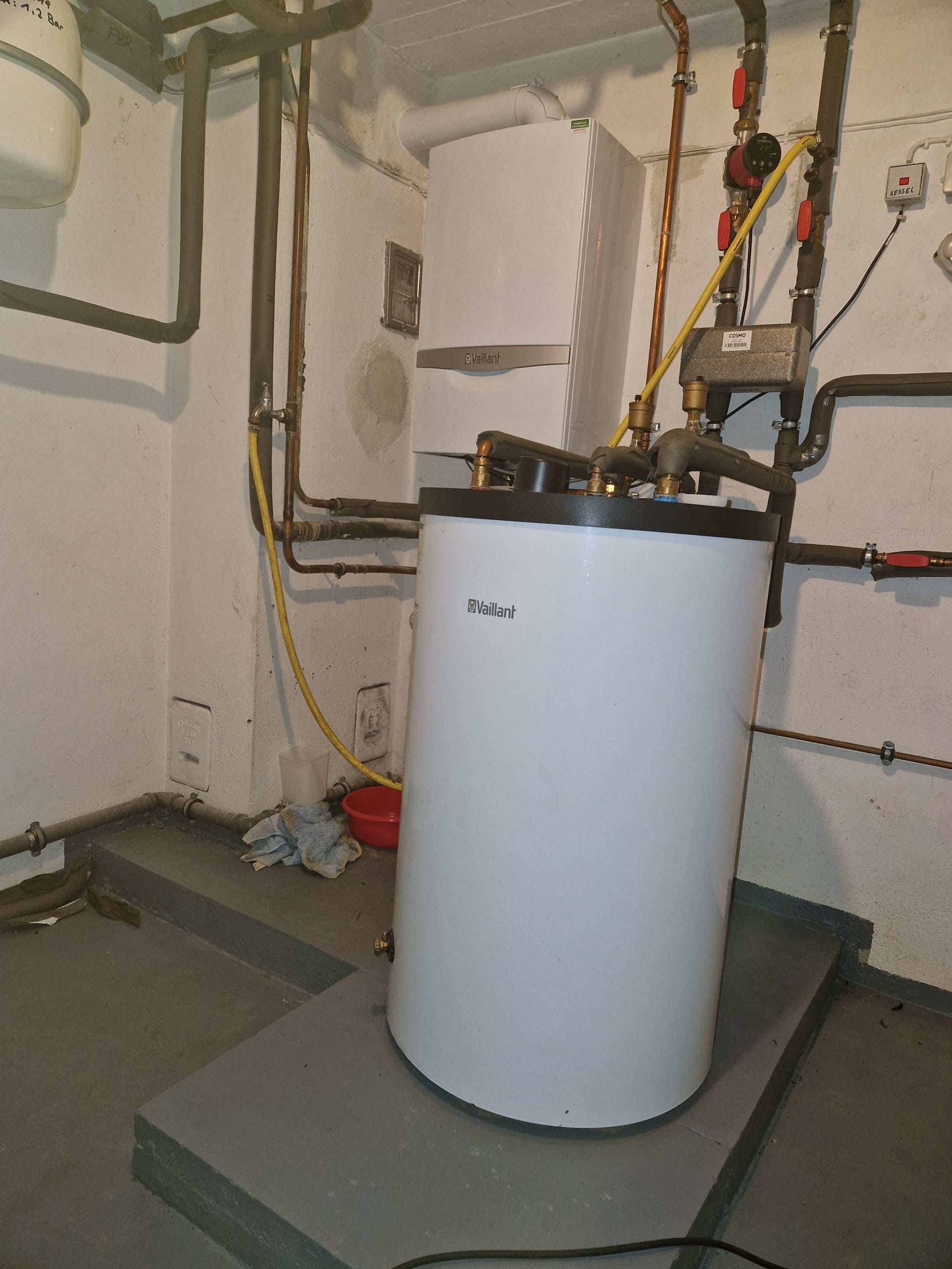 Frontalansicht einer Vaillant Gas-Brennwerttherme mit integriertem Warmwasserspeicher und sichtbaren Rohrleitungen im Keller