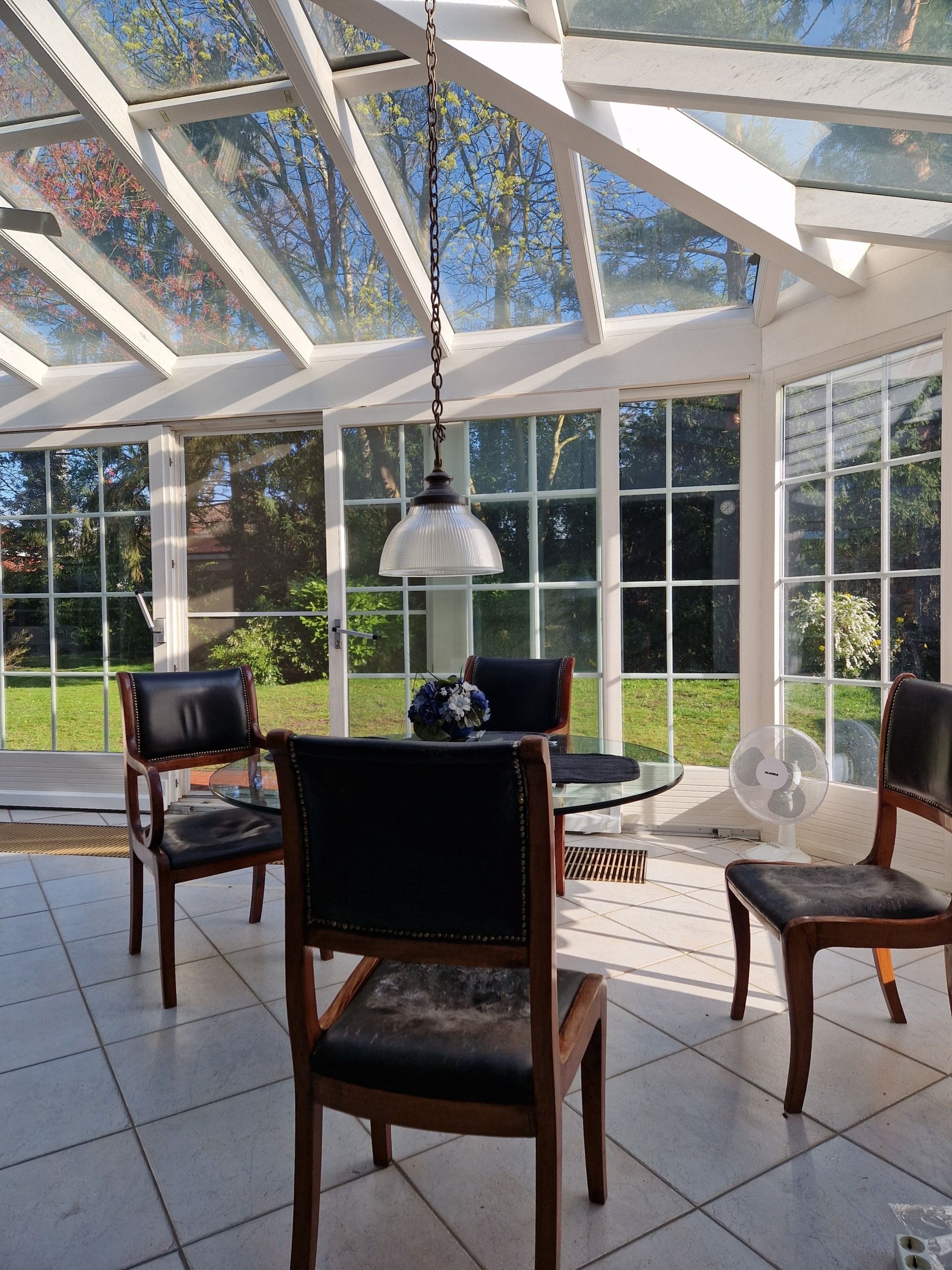 Wintergarten von innen mit Glasdach rundem Glastisch Holzstühlen und Blick in den Garten