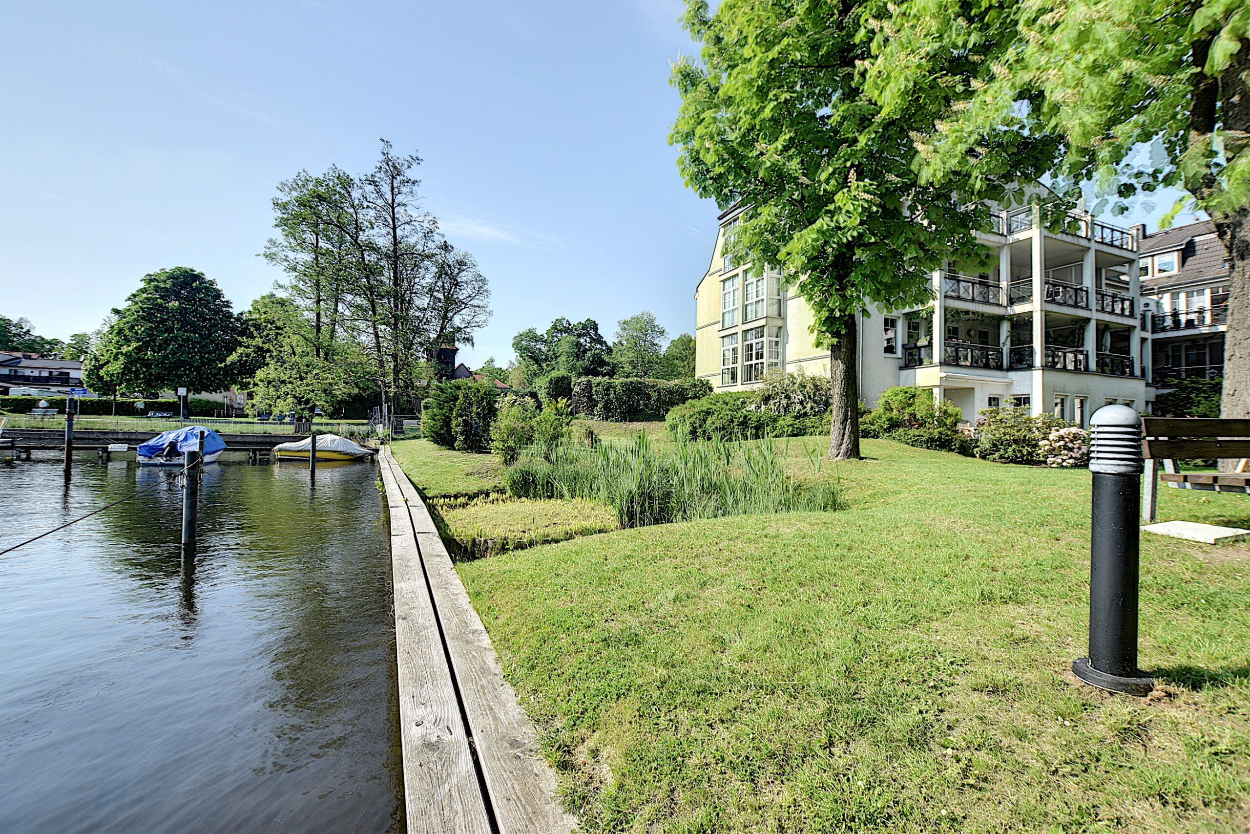 Mehrfamilienhaus in Uferlage aus Frontalperspektive mit Balkonen Rasen und Bootssteg