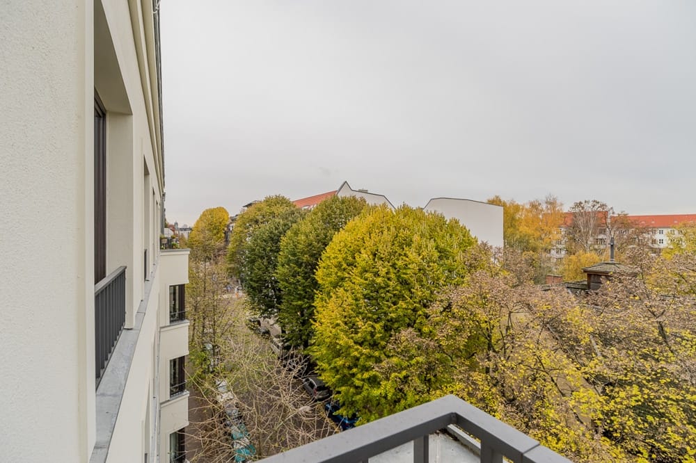 Widok z balkonu nowoczesnego, białego budynku wielorodzinnego z metalową balustradą na jesienną, kolorową aleję drzew