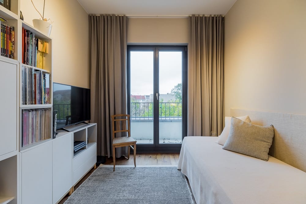 Wnętrze mieszkania z sofą, szafką pod telewizor i oknami sięgającymi podłogi, wychodzącymi na balkon