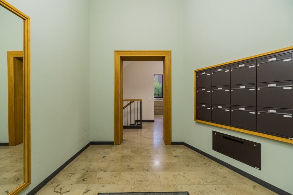 Hol wejściowy budynku wielorodzinnego z skrzynkami pocztowymi w ścianach, podłogą z piaskowca, lustrem i klatką schodową w tle