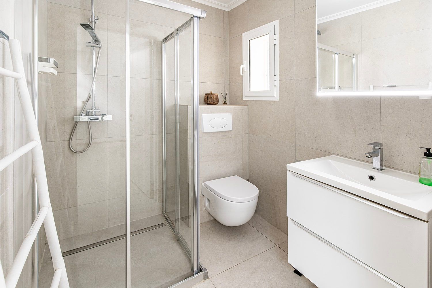 Binnenaanzicht van een moderne badkamer met een in de vloer verzonken glazen douchecabine, een aan de wand bevestigd toilet en een spiegel met ledverlichting