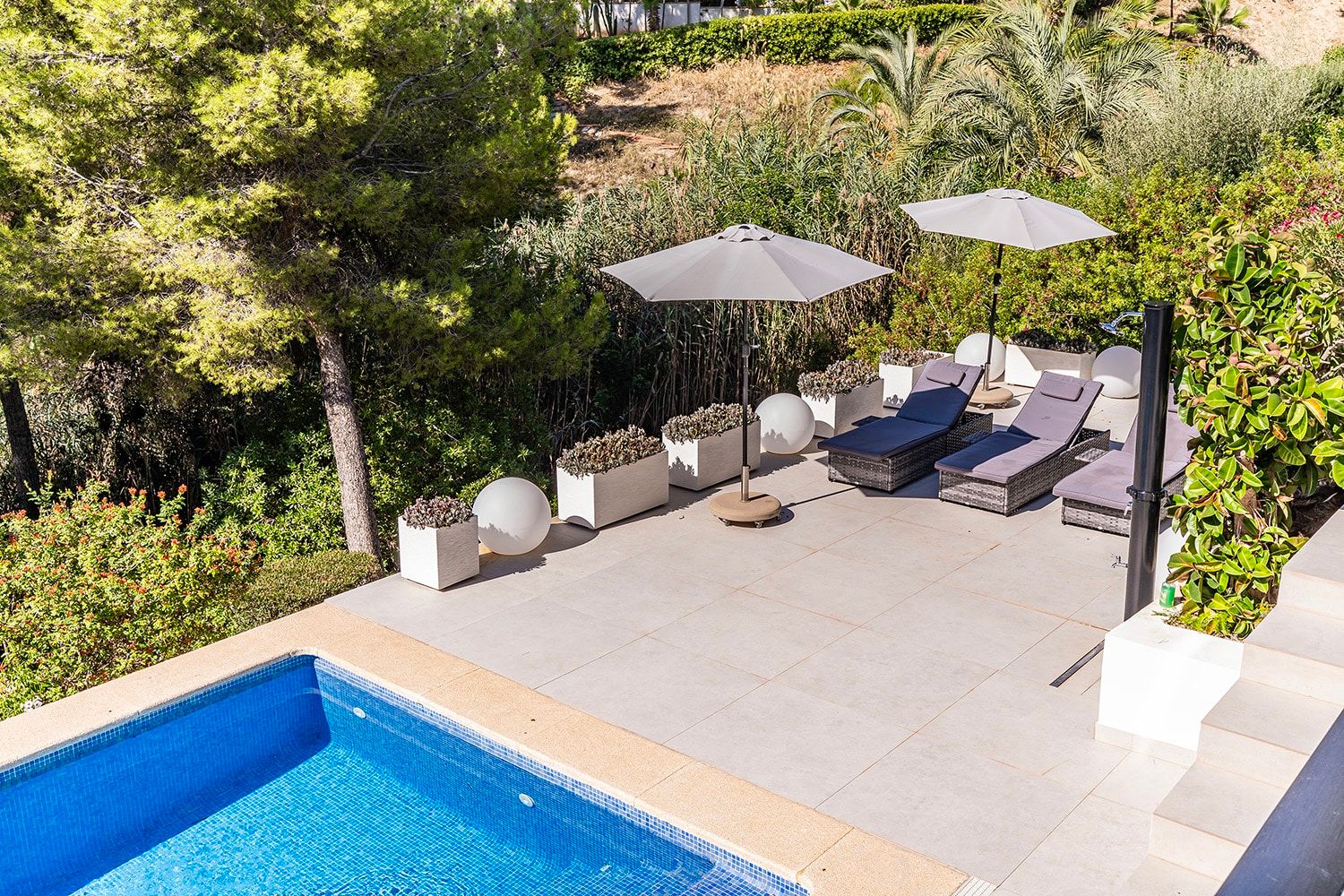 Vogelperspectief op het zwembadterras van een villa met ligstoelen, parasols en mediterrane beplanting