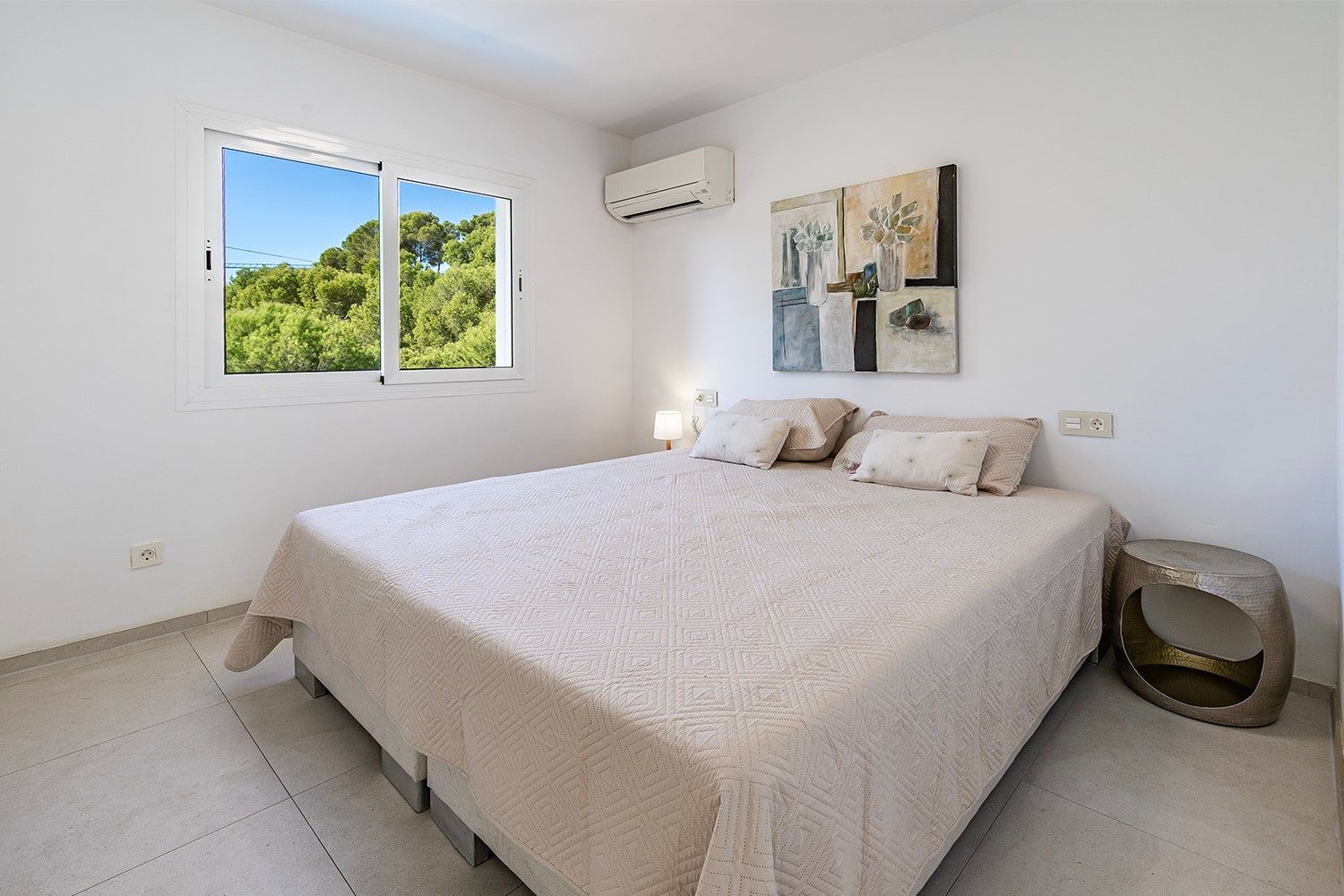 Moderne slaapkamer met tweepersoonsbed, gezien vanuit een schuin binnenperspectief; raam met uitzicht op het groen; airconditioner aan de muur