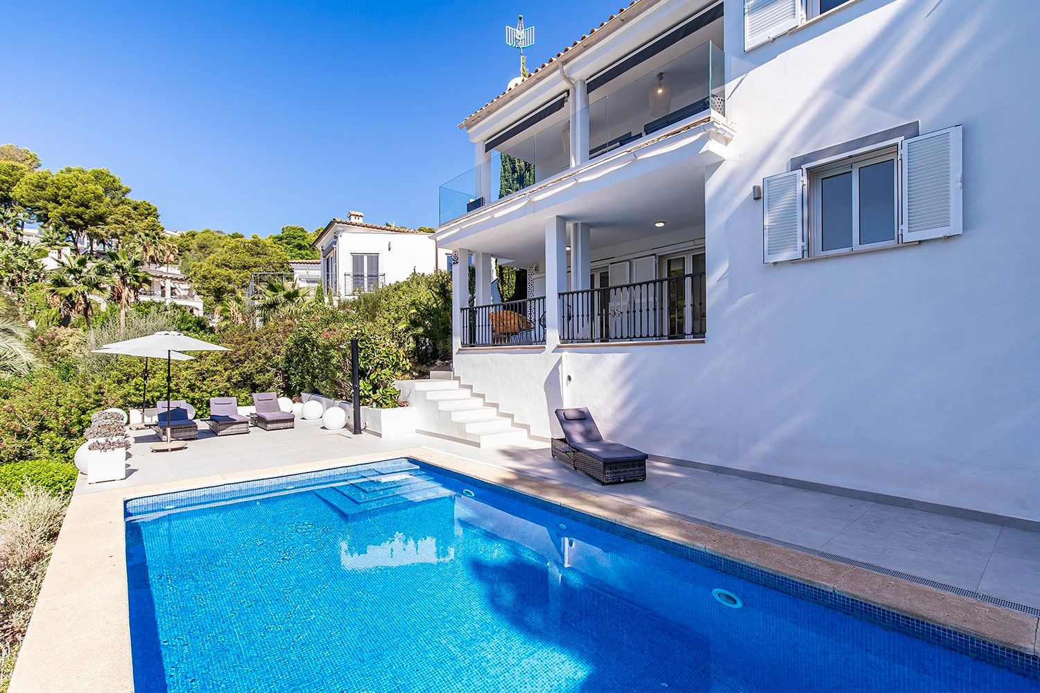 Wit gepleisterde villa met zwembad en zonneterras, gezien vanuit de zijkant, met een overdekt balkon