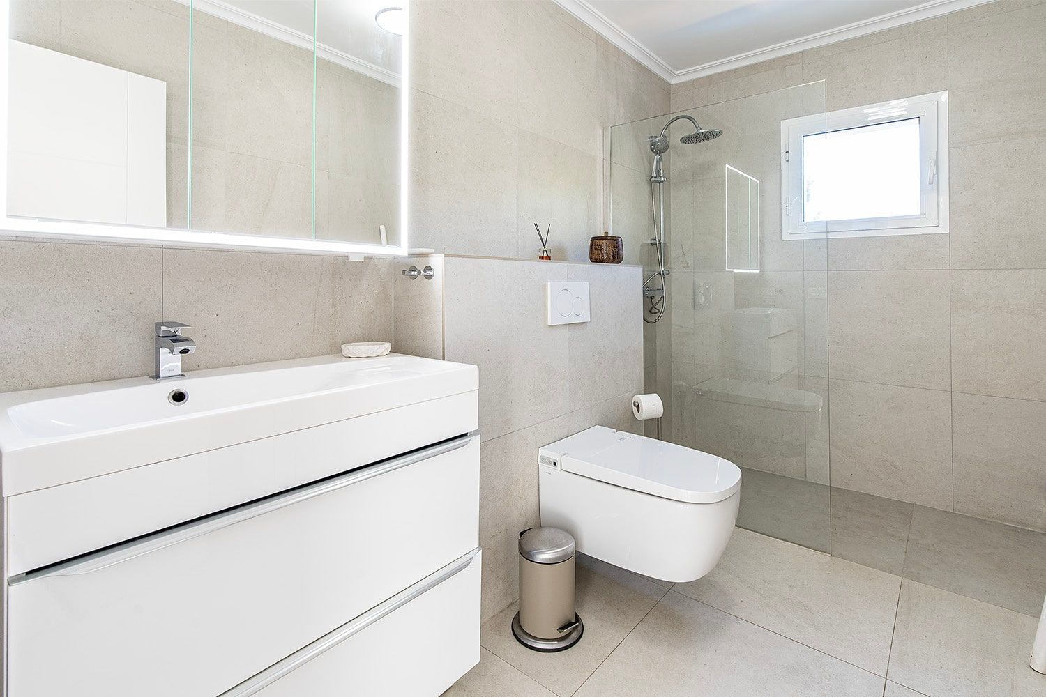 Binnenaanzicht van een moderne badkamer met natuursteentegels, een witte wastafel, een wandhangend toilet en een glazen douchecabine