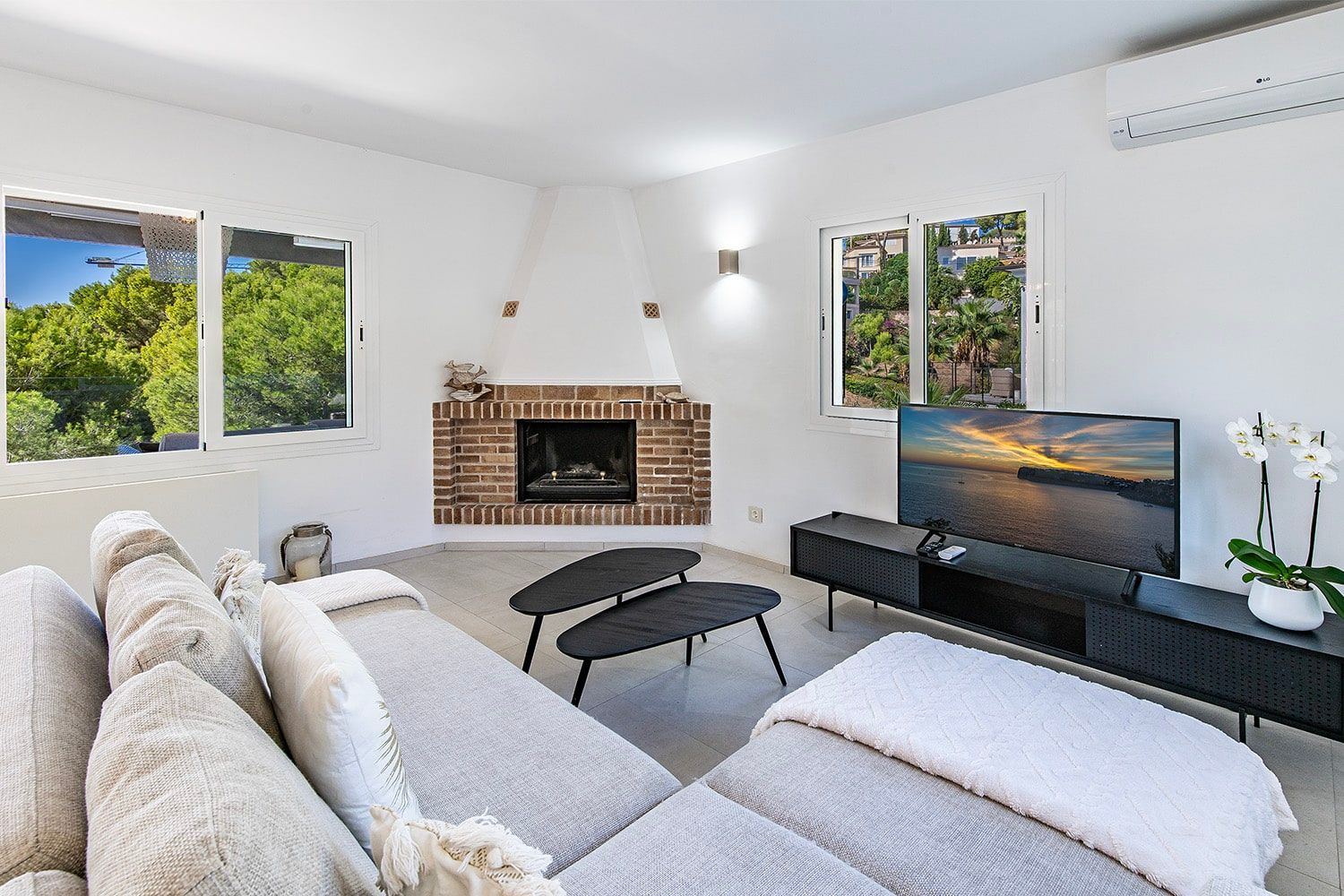 Interieur van een moderne woonkamer met een bakstenen open haard, een hoekbank, panoramavensters met uitzicht op het groen en een tv-dressoir
