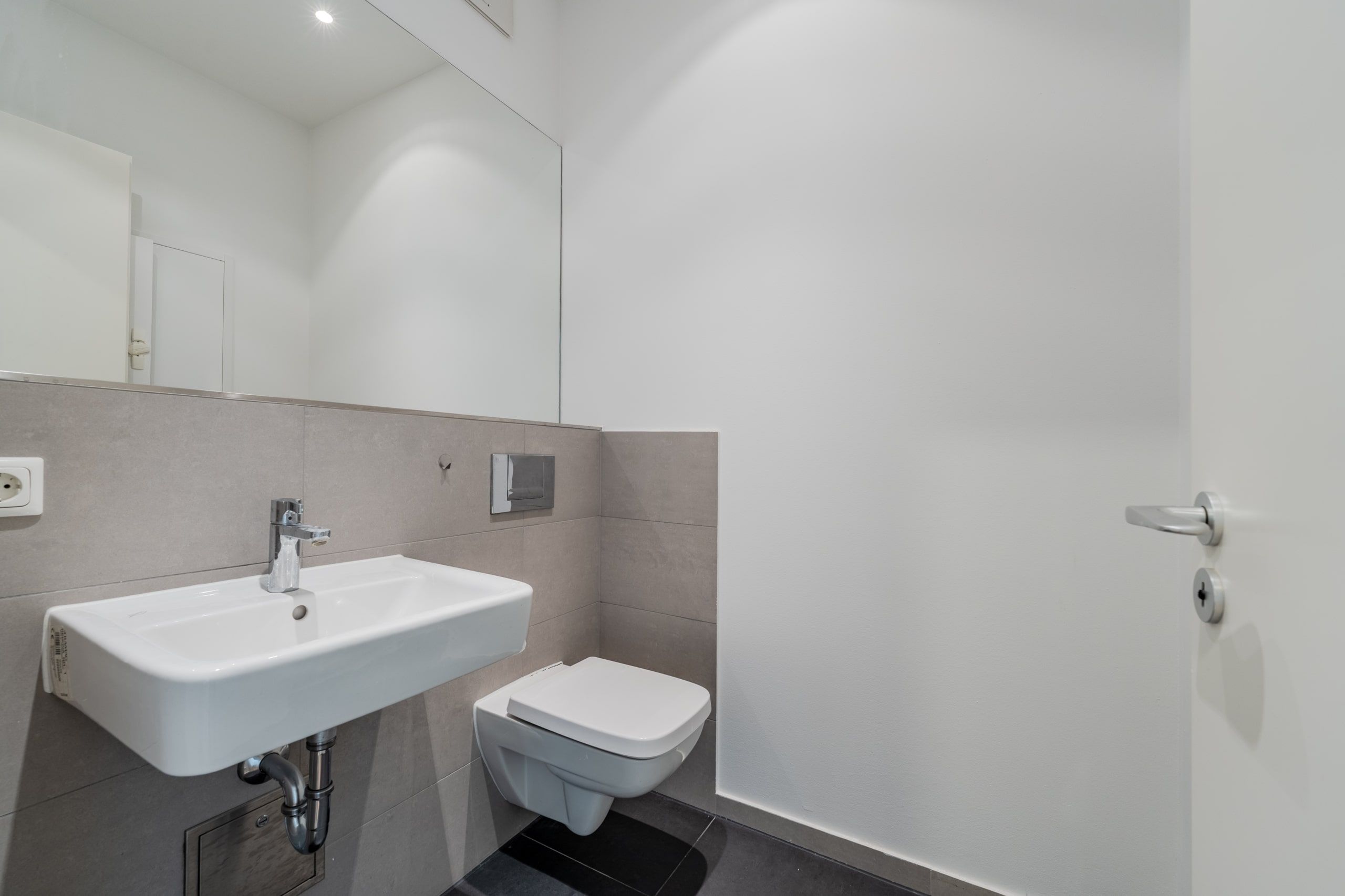Innenansicht modernes Gäste-WC mit wandhängendem Waschbecken und Toilette vor großem Spiegel
