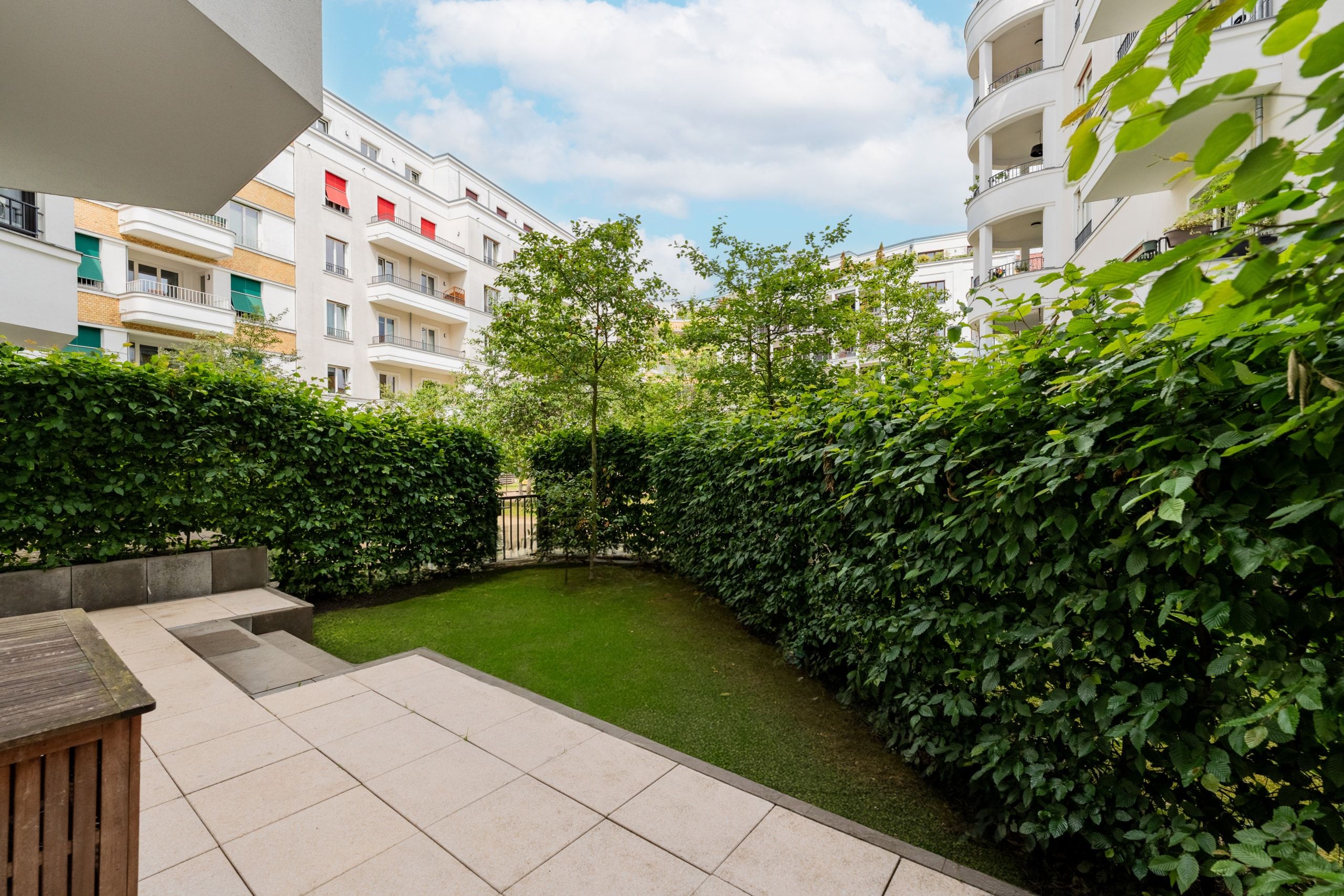 Blick von Terrasse auf begrünten Hof mit Hecke und umlaufenden mehrstöckigen Wohngebäuden mit Balkonen