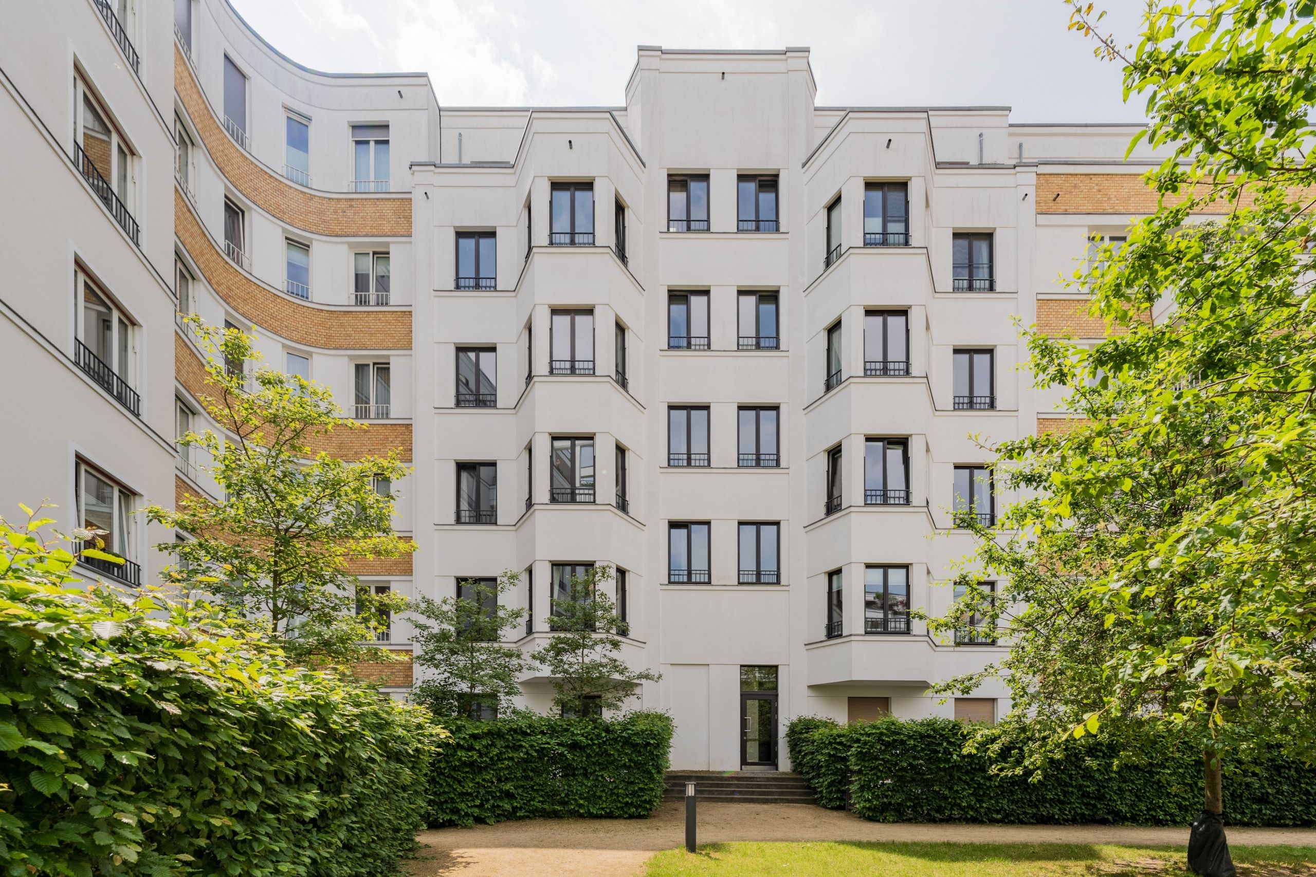 Innenhofansicht mehrstöckiges Wohnhaus mit weißer Putzfassade Klinkerakzenten und begrüntem Vorgarten
